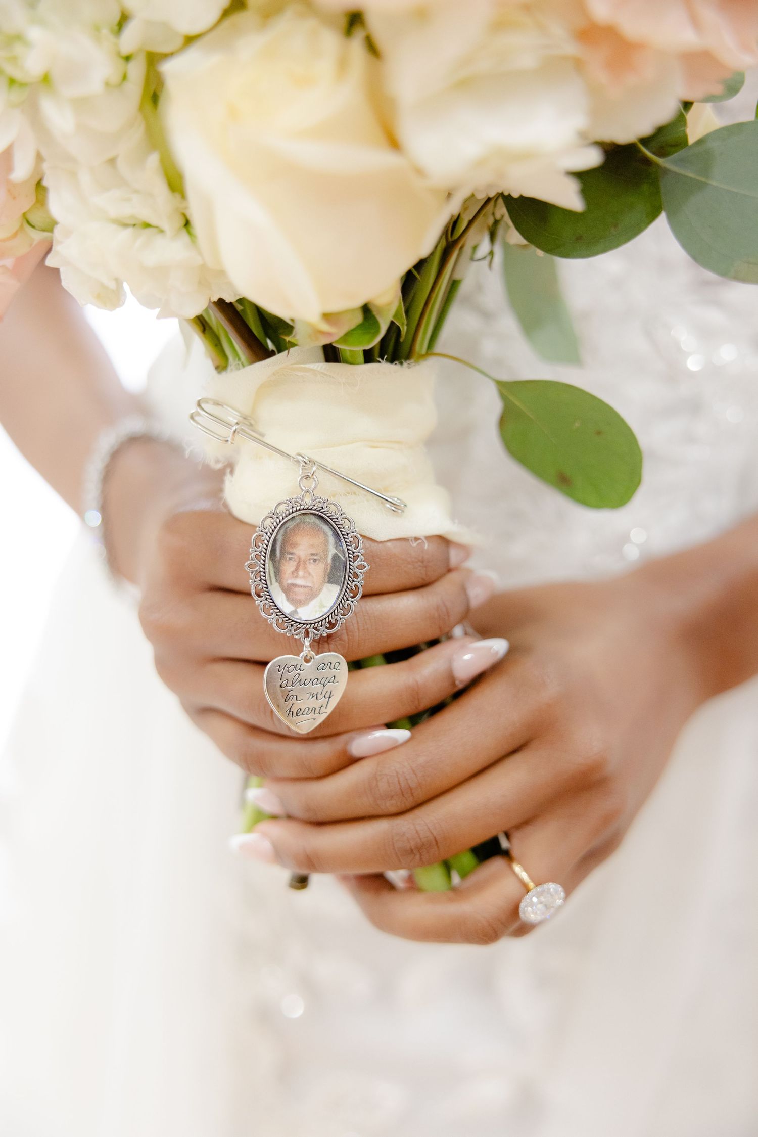 Wedding bouquet held with sentimental photo locket and rings detail shot.