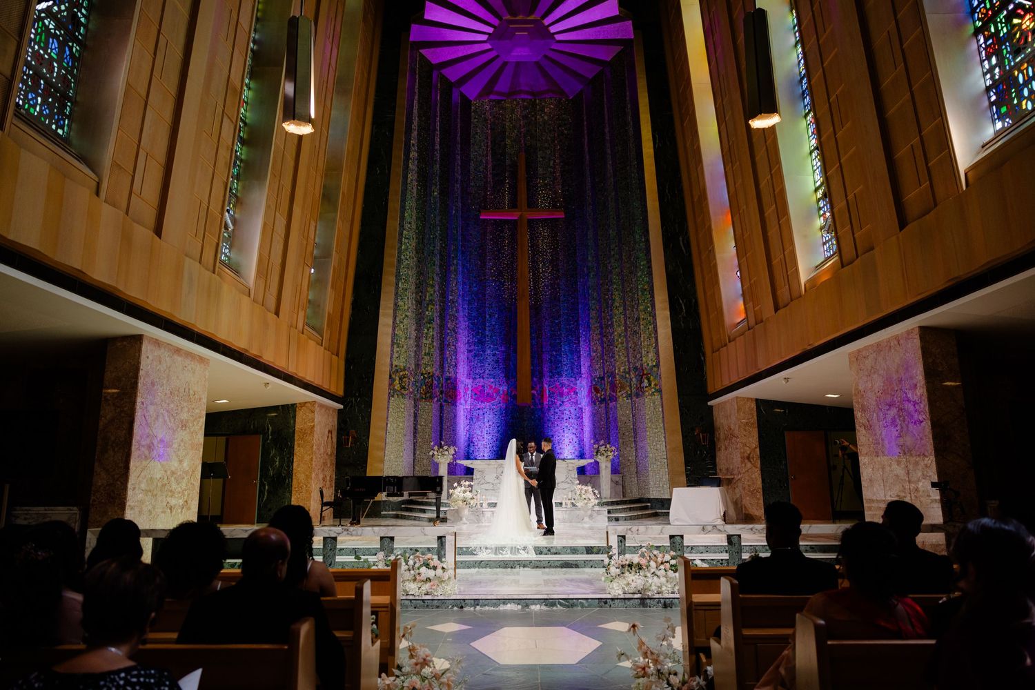A church altar illuminated with dramatic purple lighting and a cross centerpiece during a wedding ceremony.