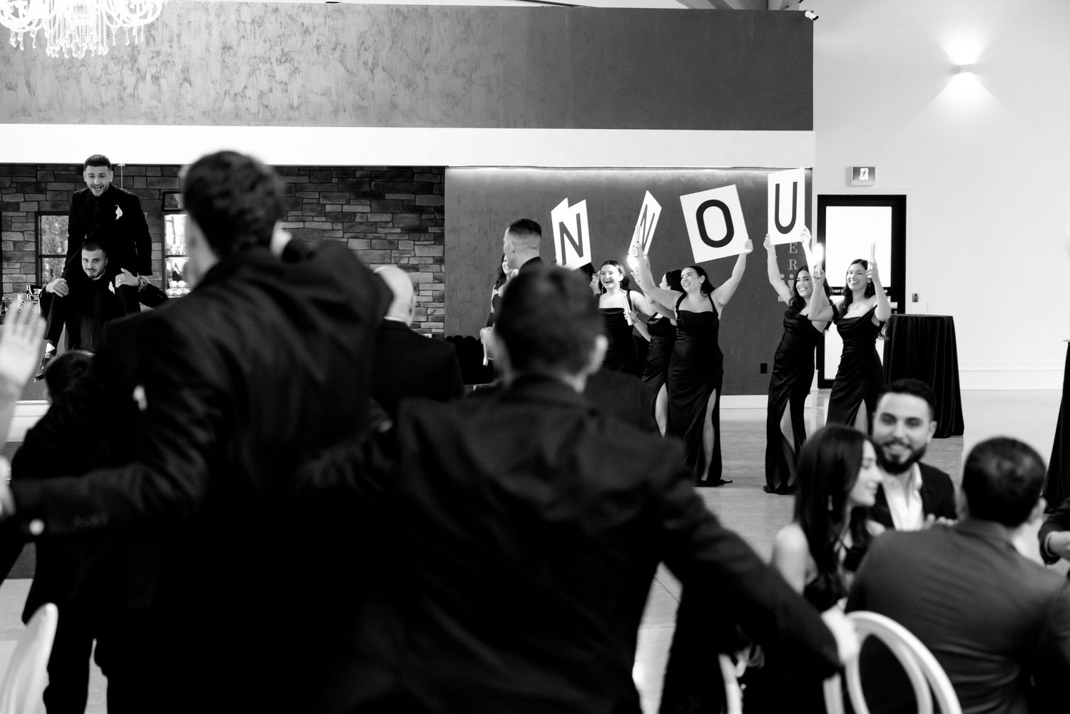 Black and white photo of wedding guests holding up letter signs during a reception celebration.