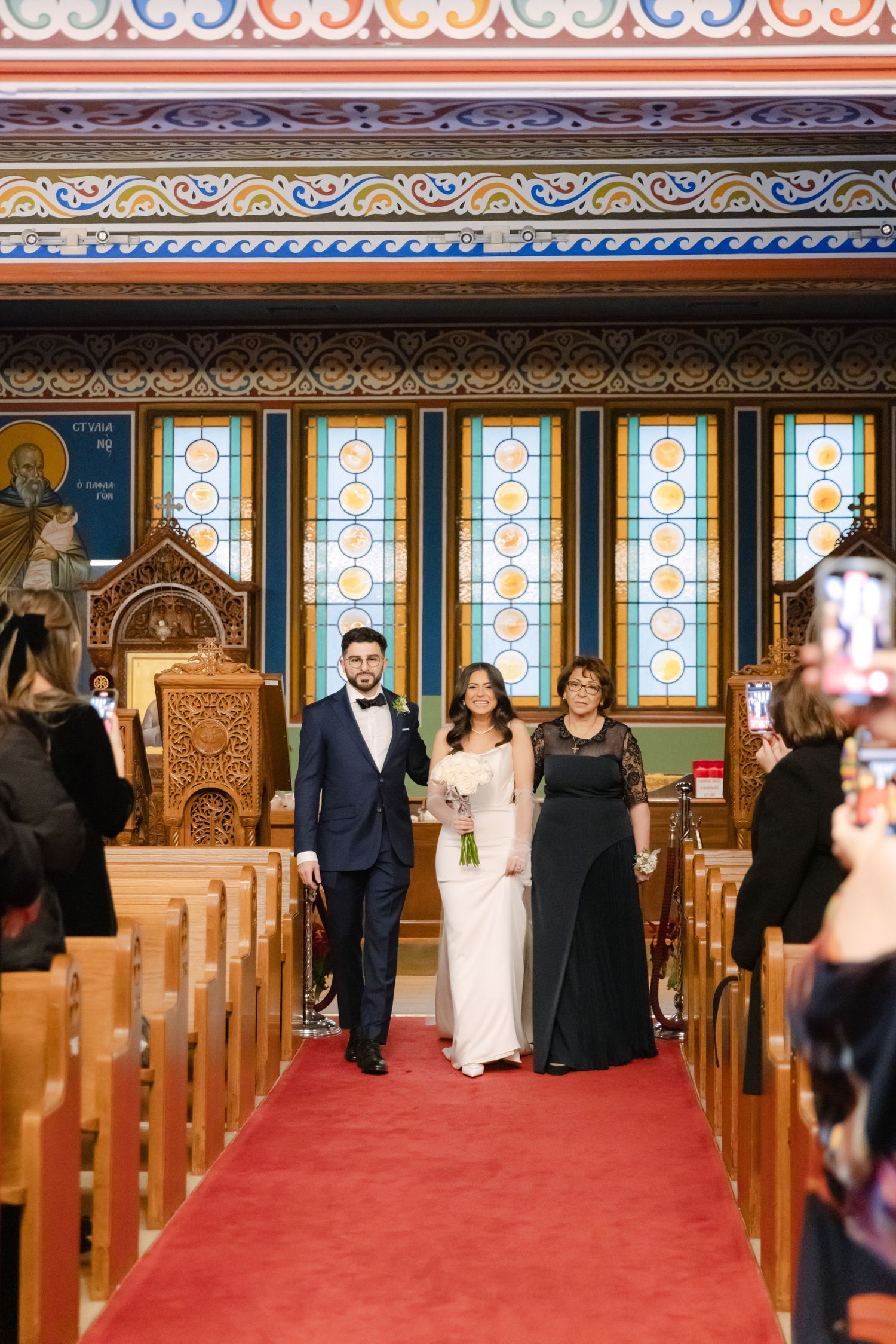Wedding processional in an ornate church with stained glass windows and red carpet aisle.