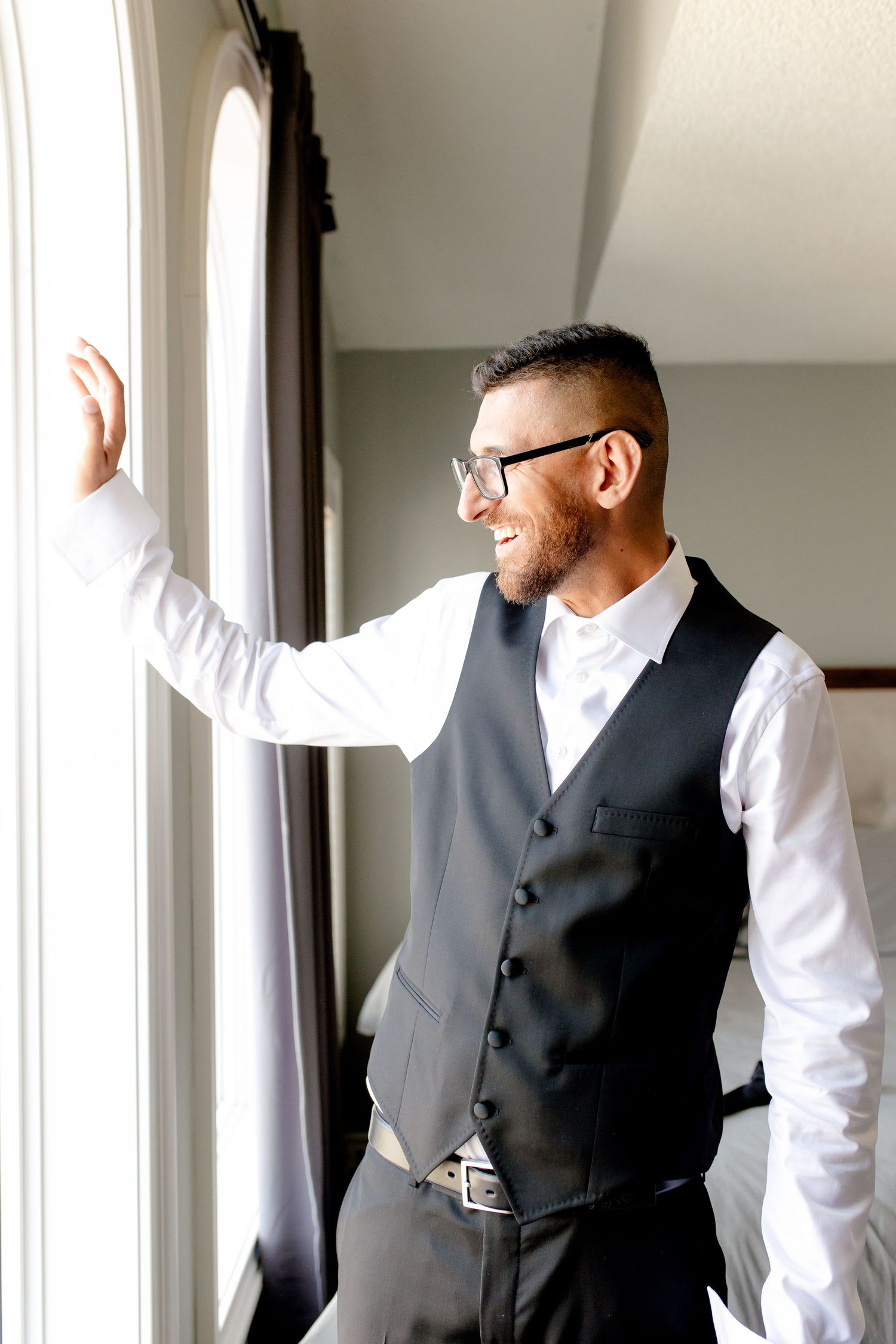 A person in formal attire smiles while standing near a window in natural light.