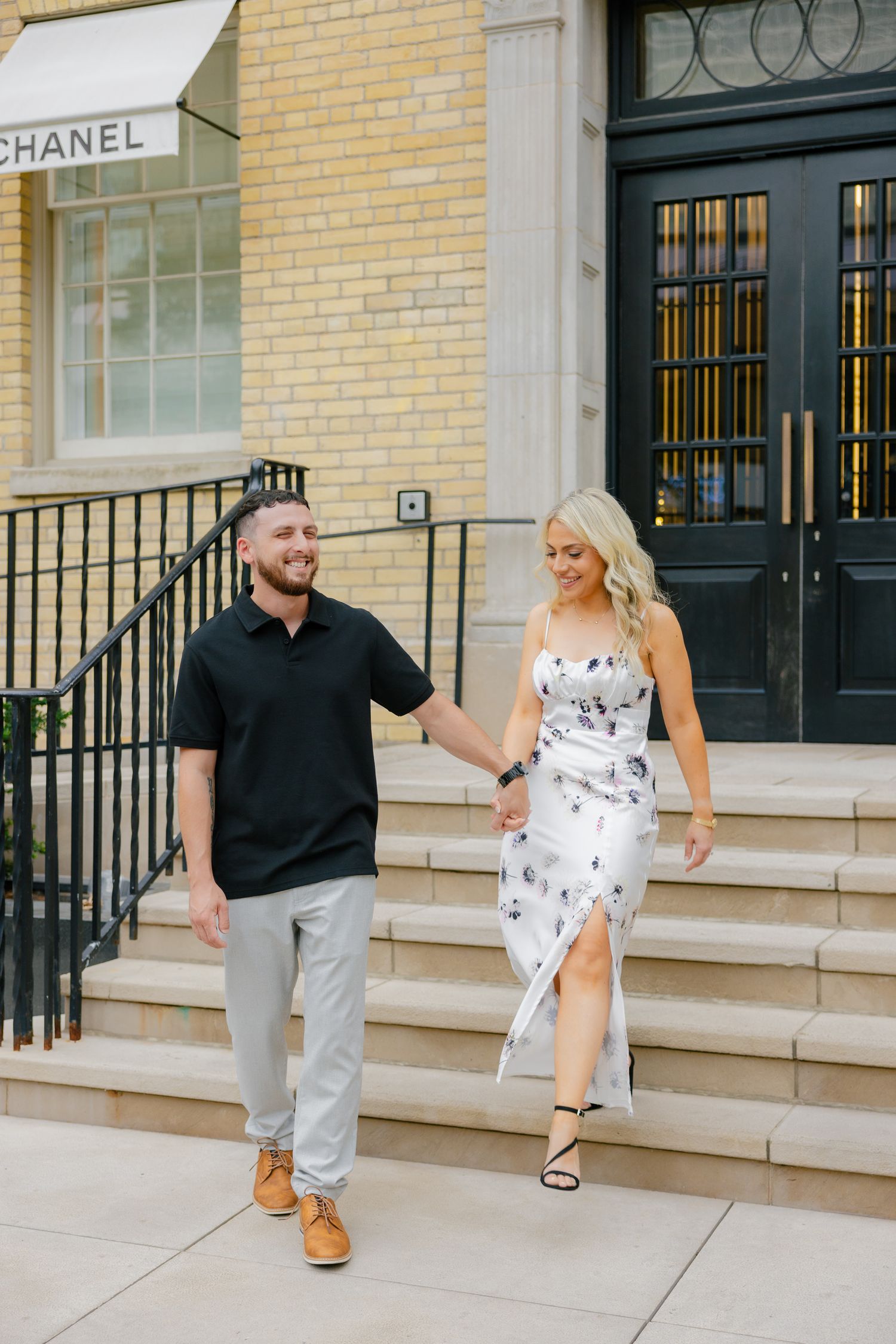 Happy couple walking down Chanel boutique steps in complementary casual outfits.