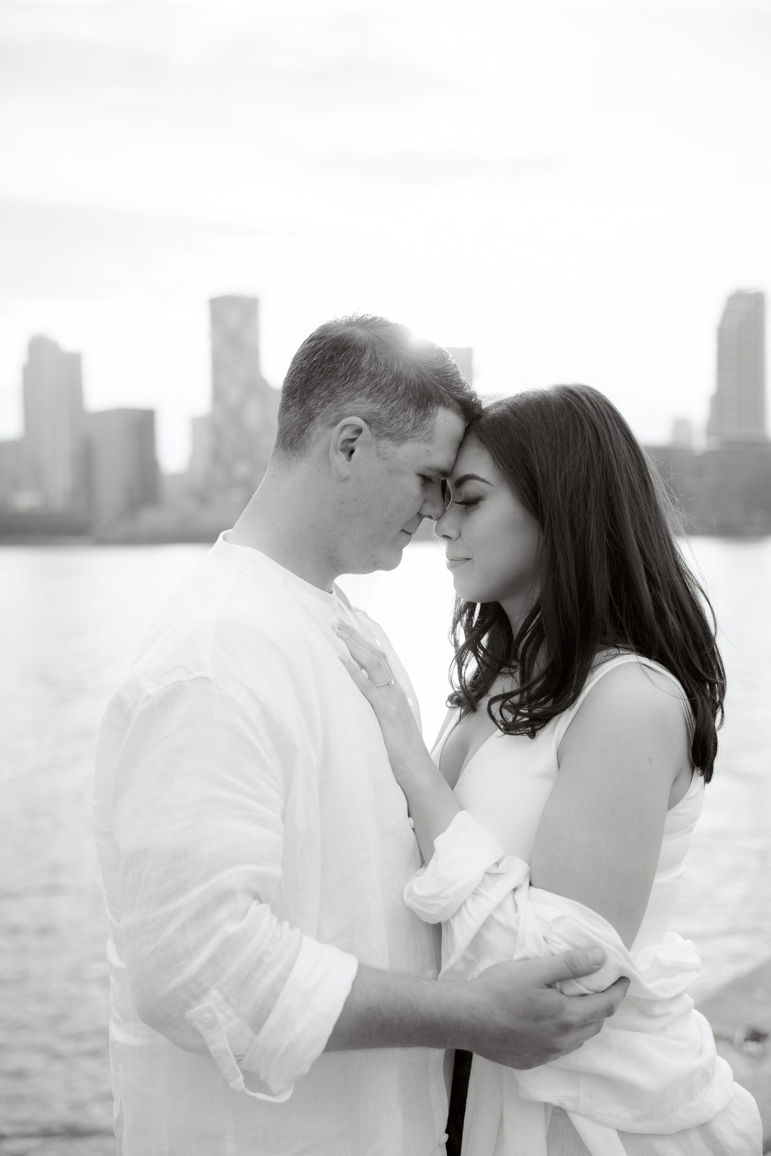 An intimate black and white portrait of a couple sharing a tender moment by the waterfront.