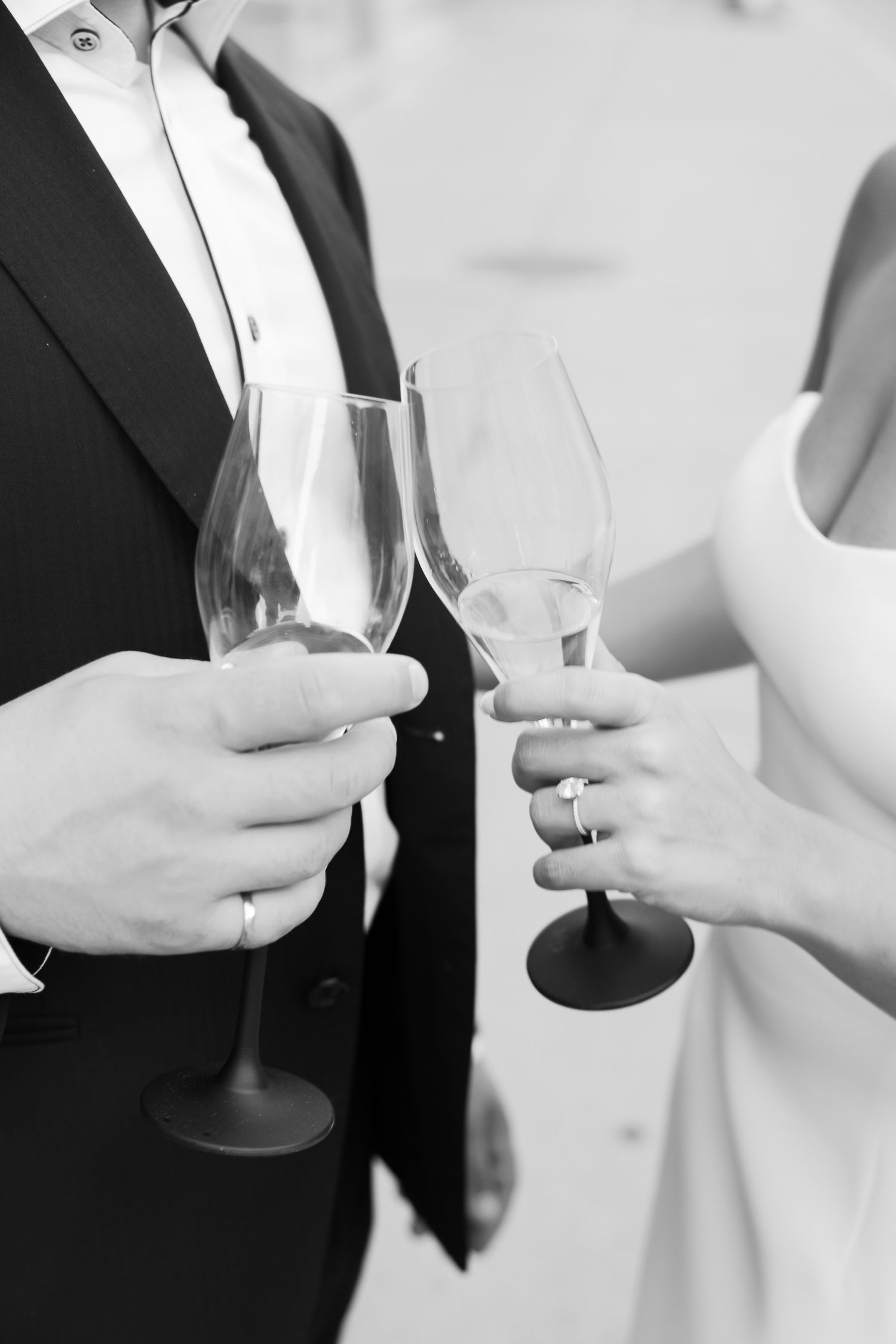 Close-up of champagne glasses held by couple in formal black and white attire.