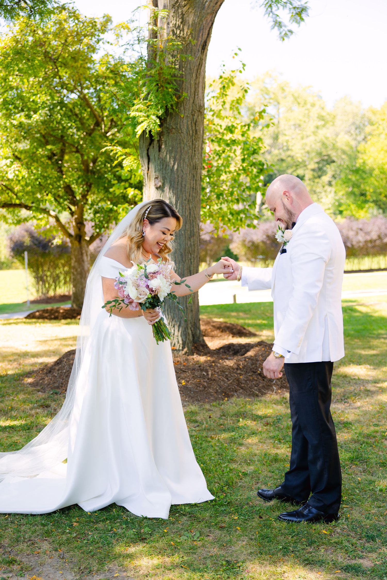 Wedding couple sharing a sweet moment under a tree while looking at rings.