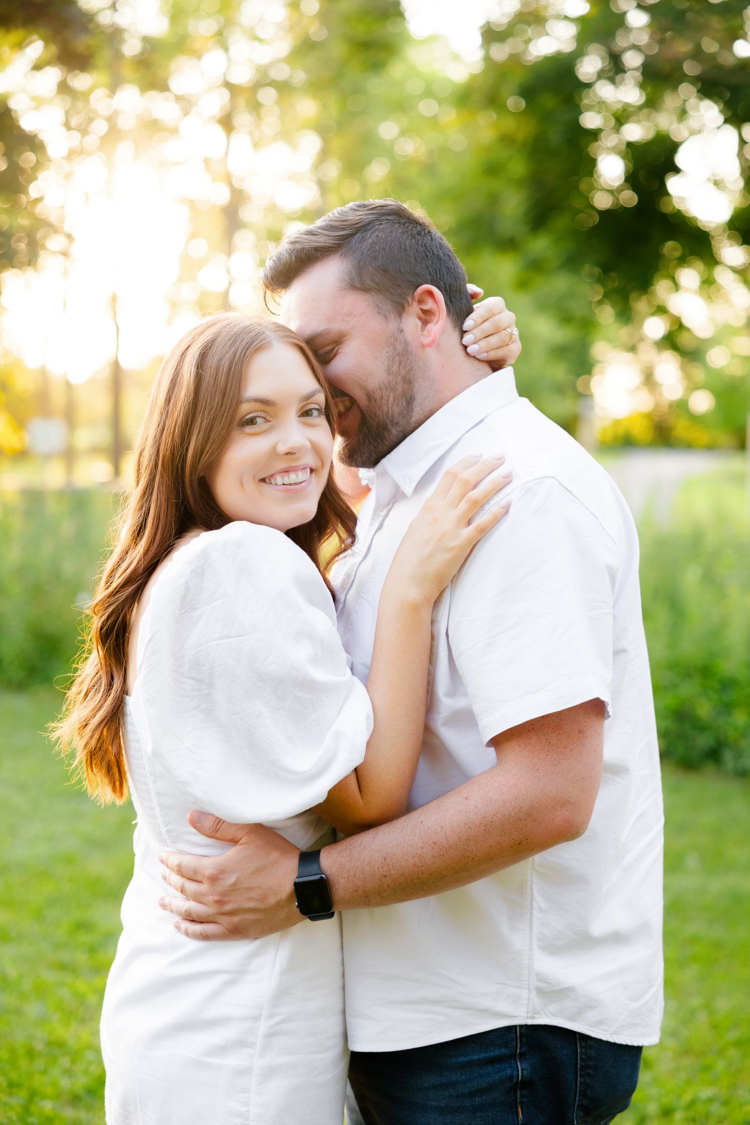 Tender moment between couple wearing white as they embrace in a sunny garden.