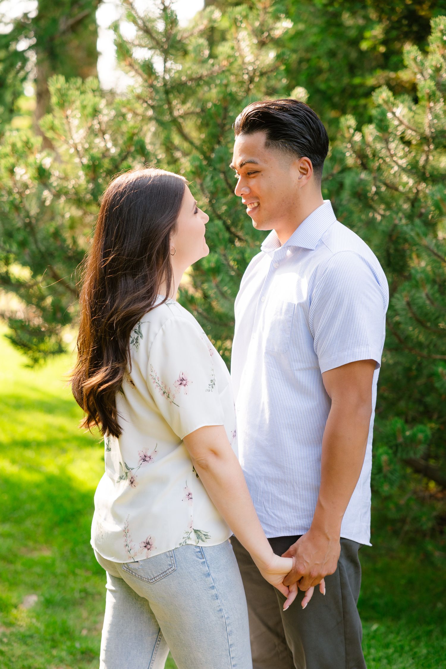 A loving couple gazes at each other while holding hands in a sunny garden surrounded by greenery.