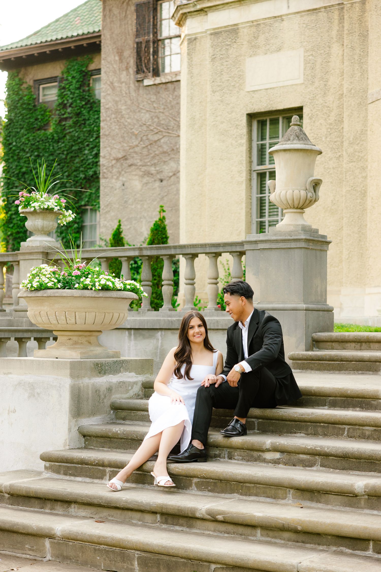 A couple in contrasting black and white outfits sits on grand stone steps of an elegant building.