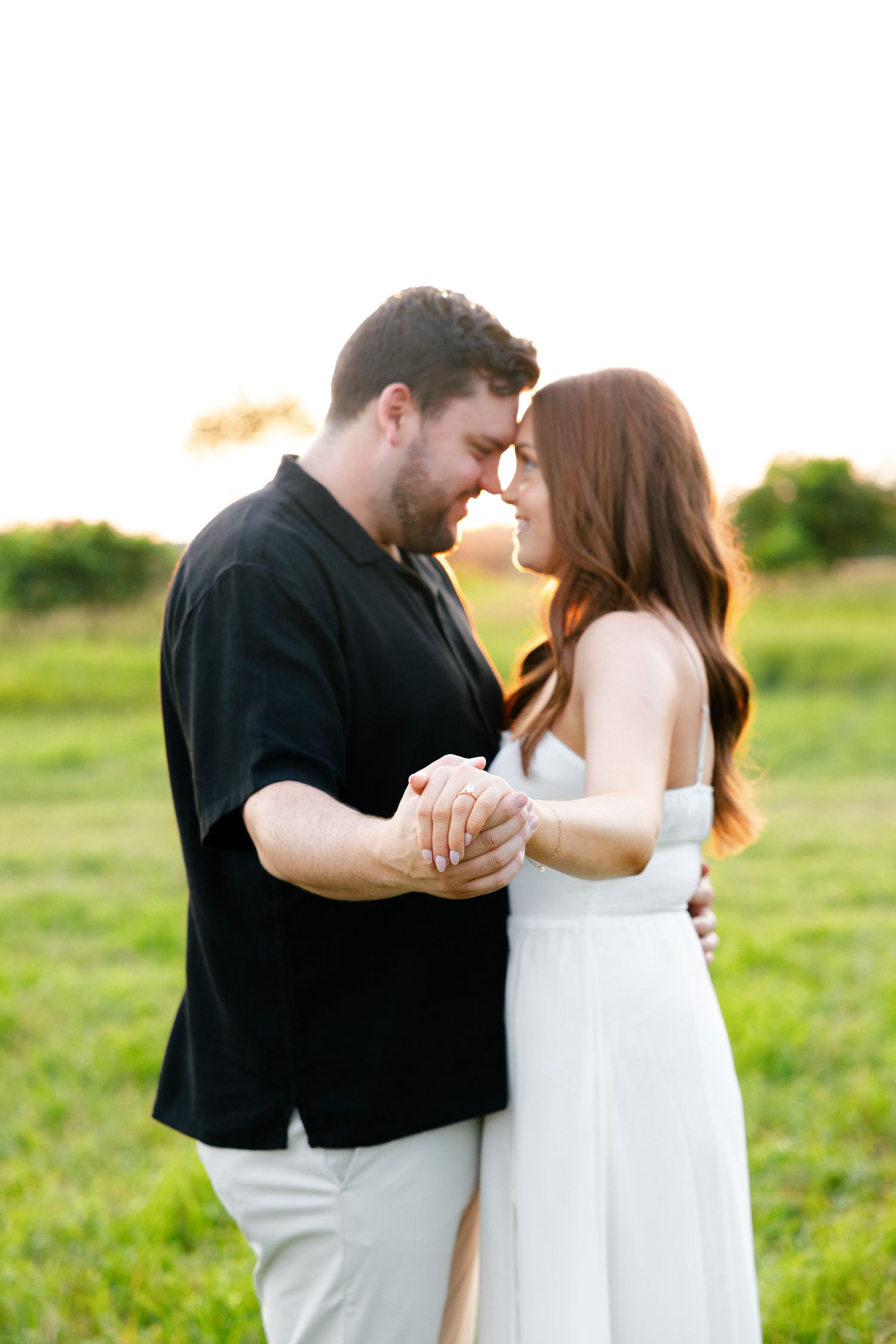 Intimate moment between couple during sunset engagement photoshoot in field.