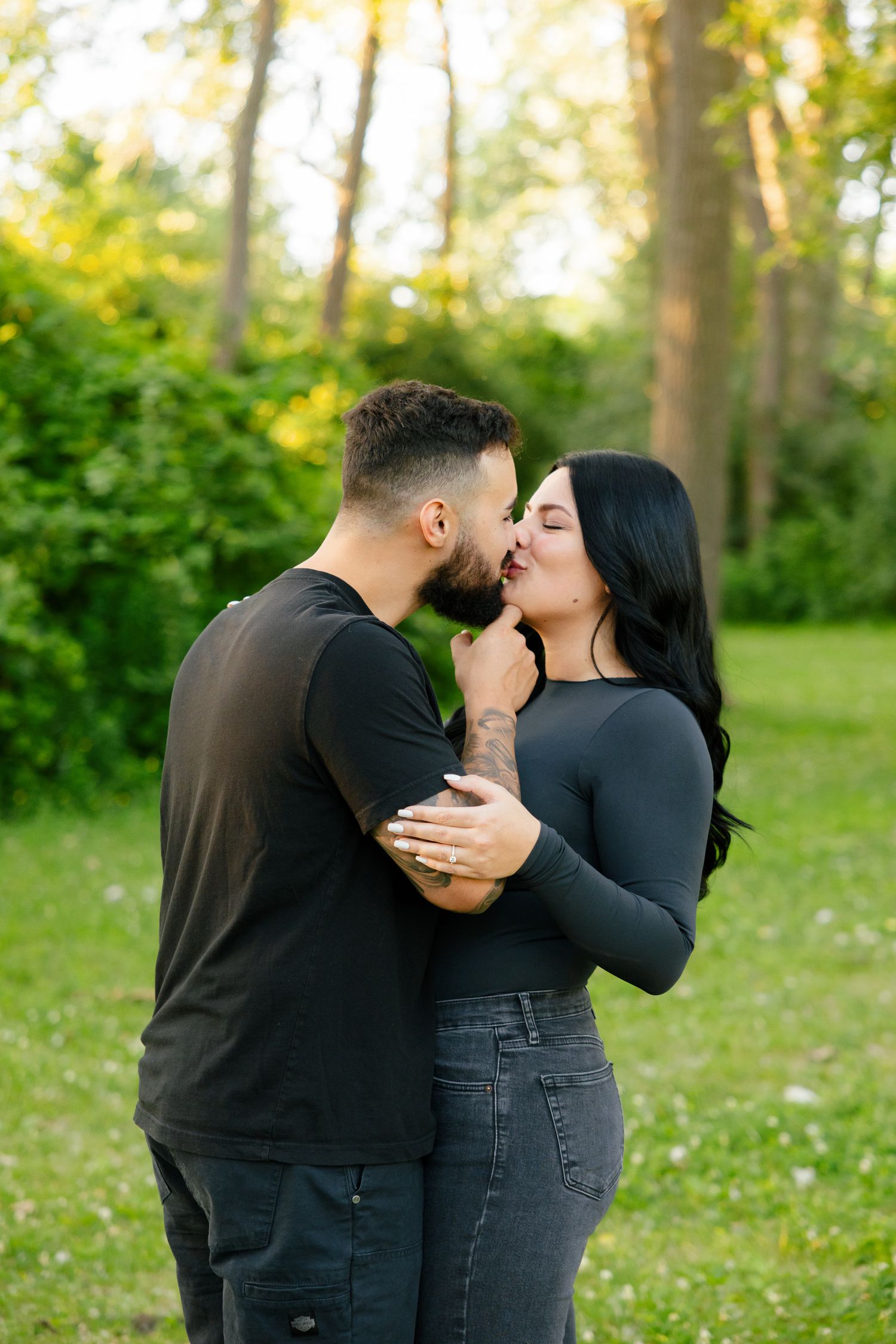 Tender moment between couple in casual black outfits against a natural woodland setting.