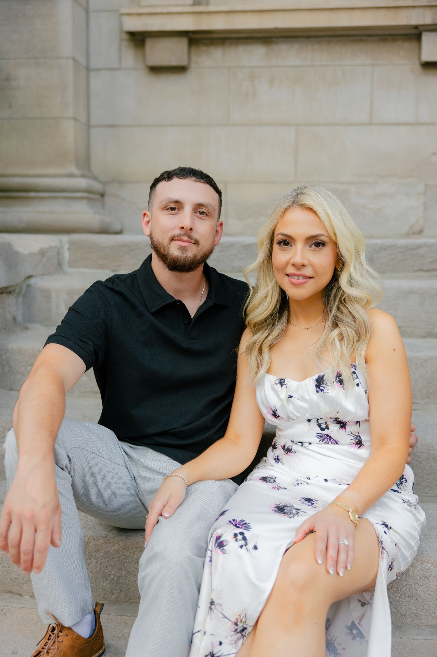 A couple poses together on stone steps wearing coordinated casual outfits.