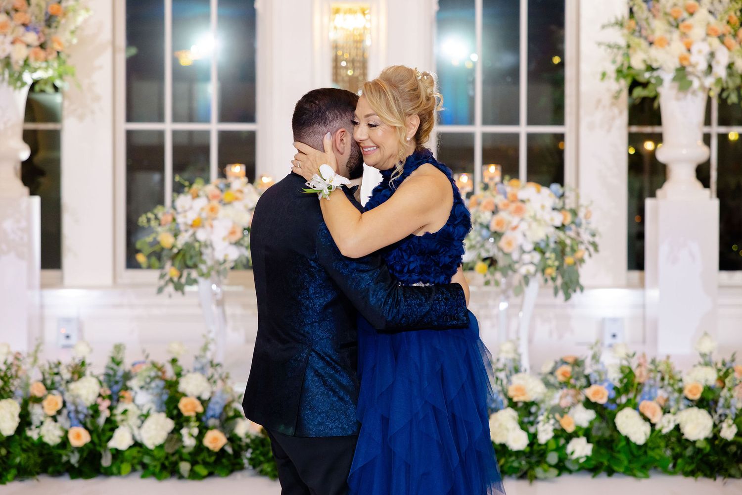 Wedding celebration dance sequence with guests in navy blue attire against white paneled walls.