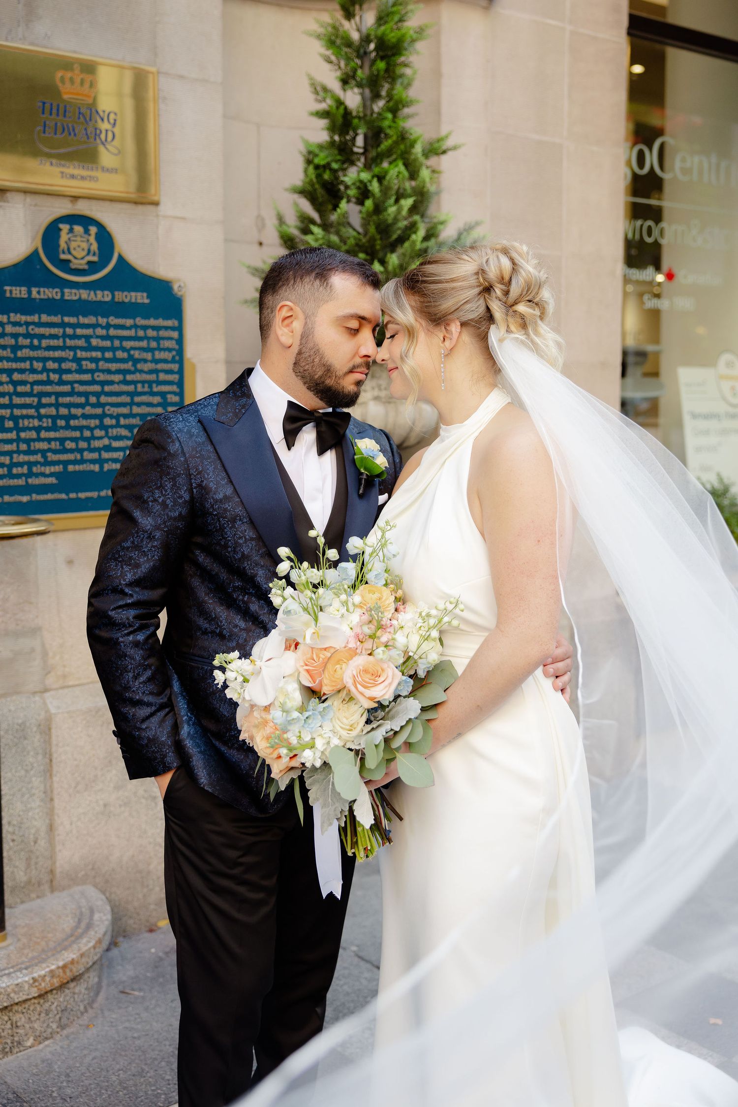 Romantic wedding portraits showing a couple in white dress and dark suit with flowing veil and peach bouquet.