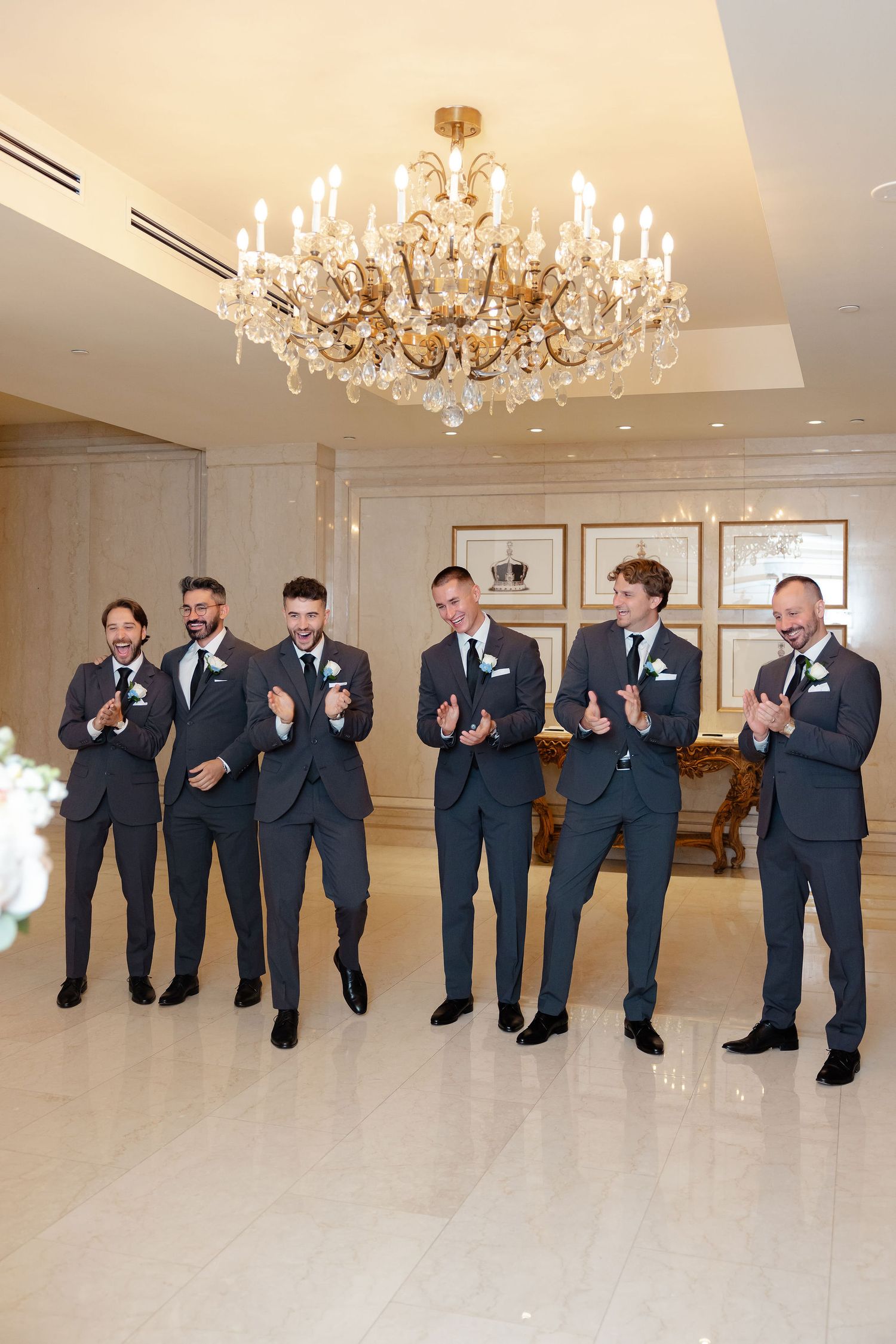 Groomsmen in navy suits perform synchronized dance moves in an elegant ballroom setting.