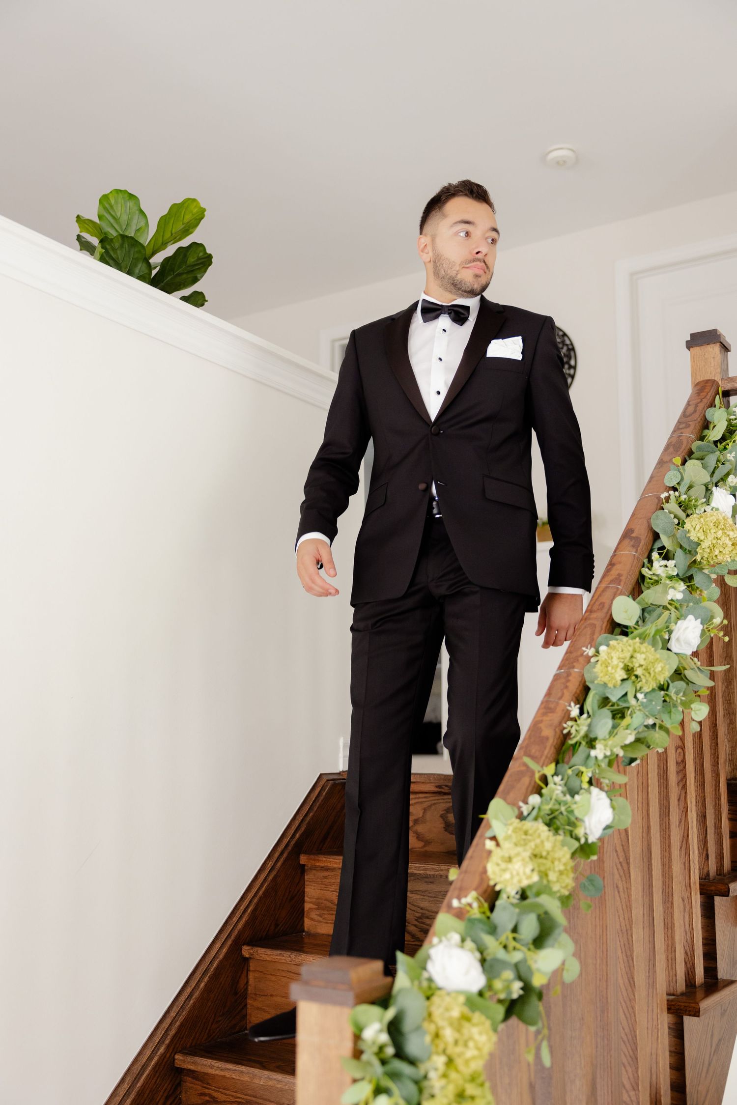 Person in tuxedo descends decorated staircase adorned with greenery and white flowers.