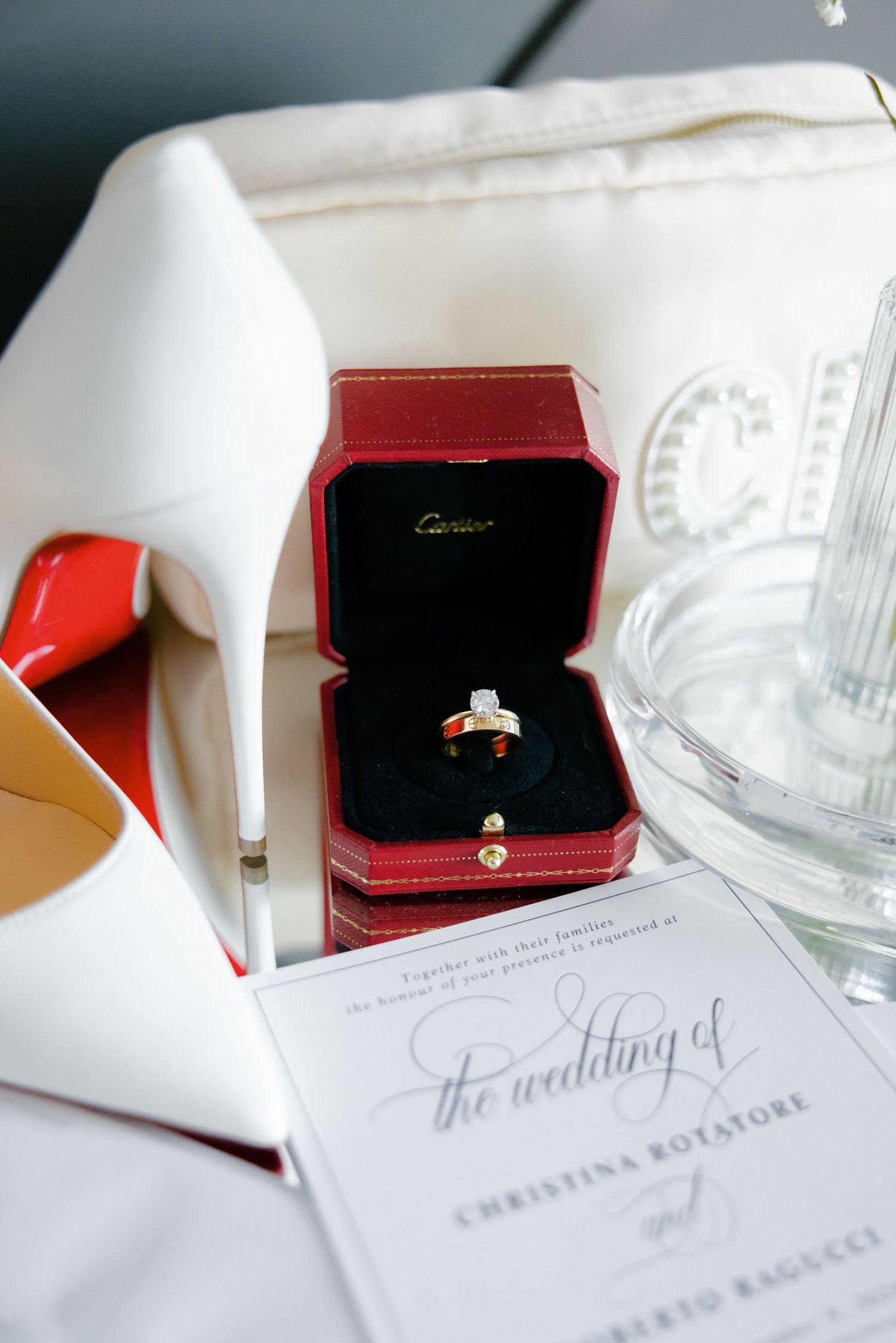 Diamond engagement ring in red Cartier box displayed with wedding invitation.