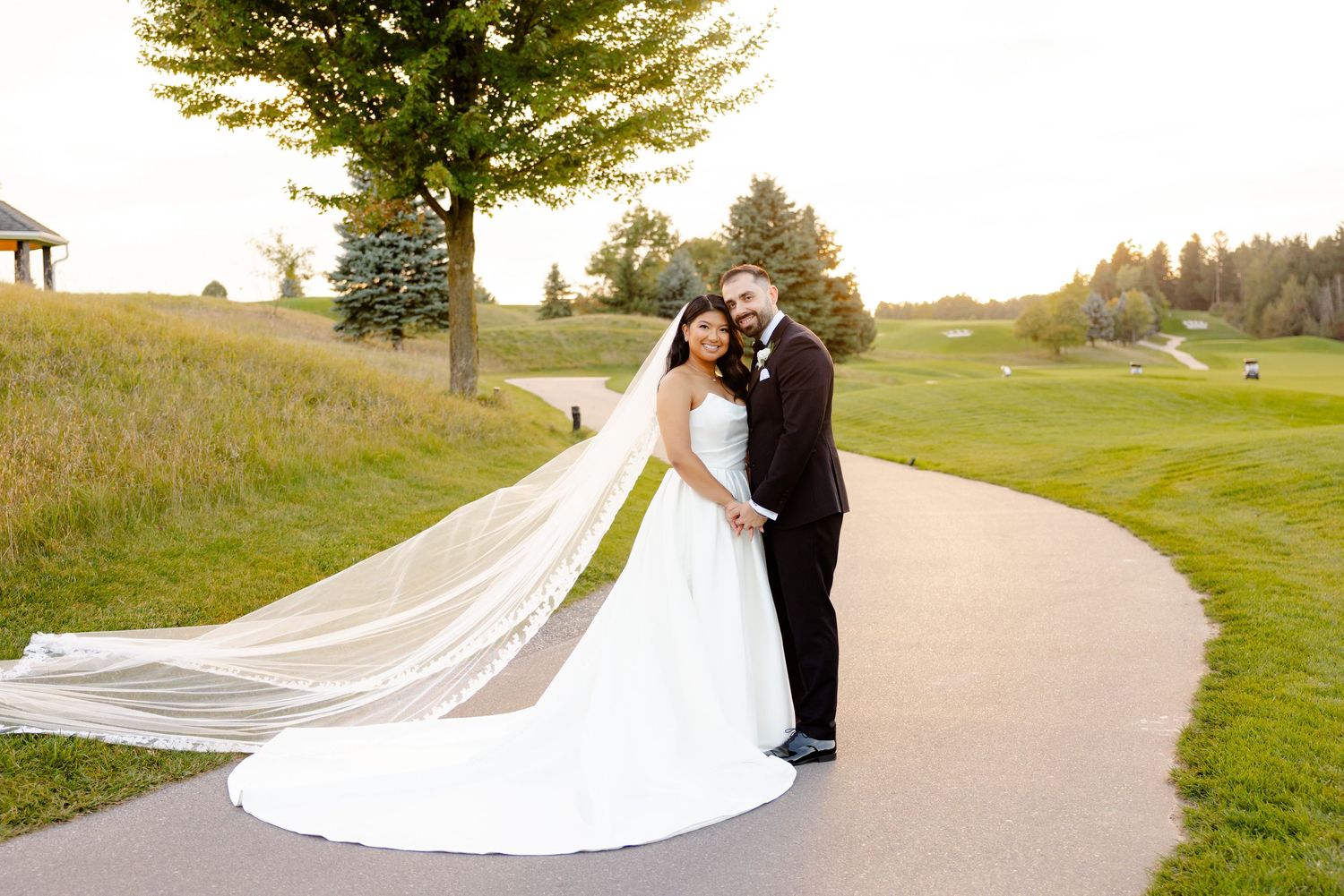 Elegant wedding portrait on a golf course path with bride's long flowing veil.