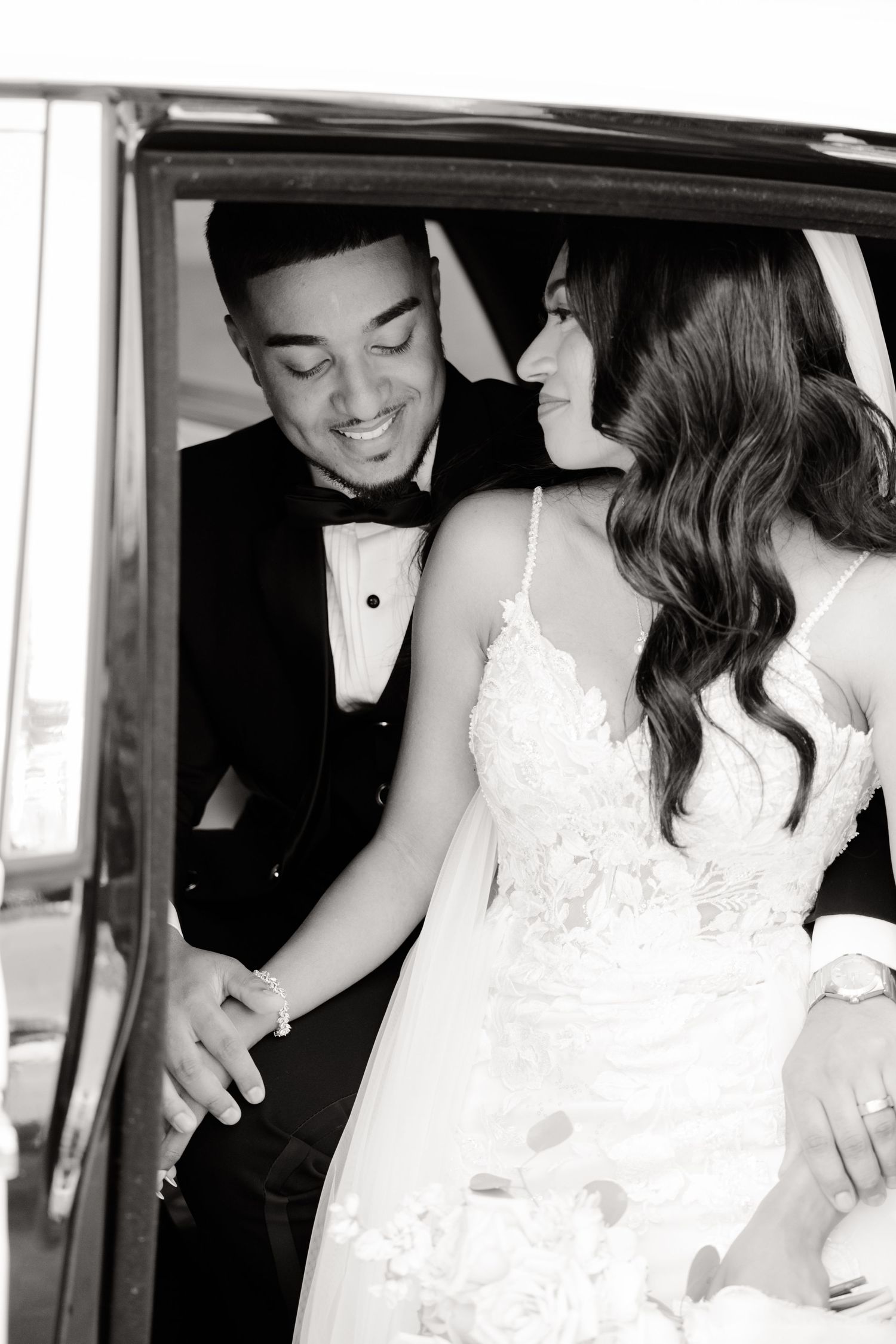 Black and white portrait of a happy couple in wedding attire inside a classic car.