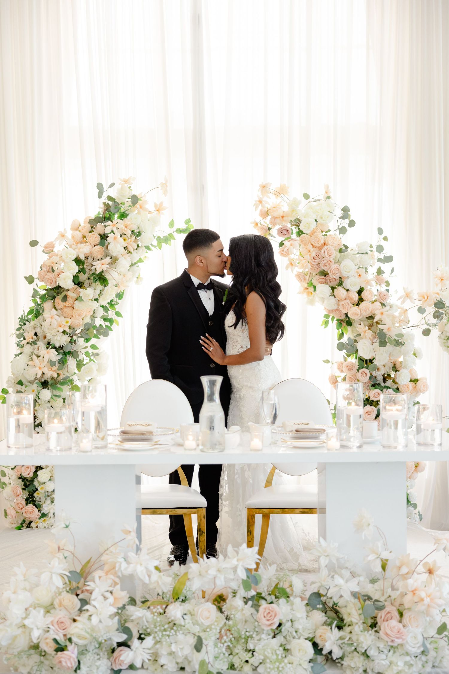 Romantic sweetheart table moment framed by pink floral arches in bright white reception space.