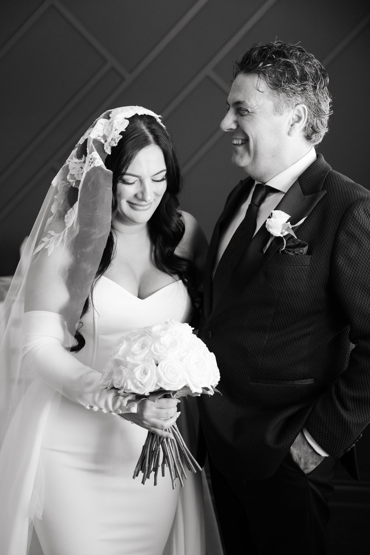 A black and white wedding portrait showing a tender moment against a patterned wall.