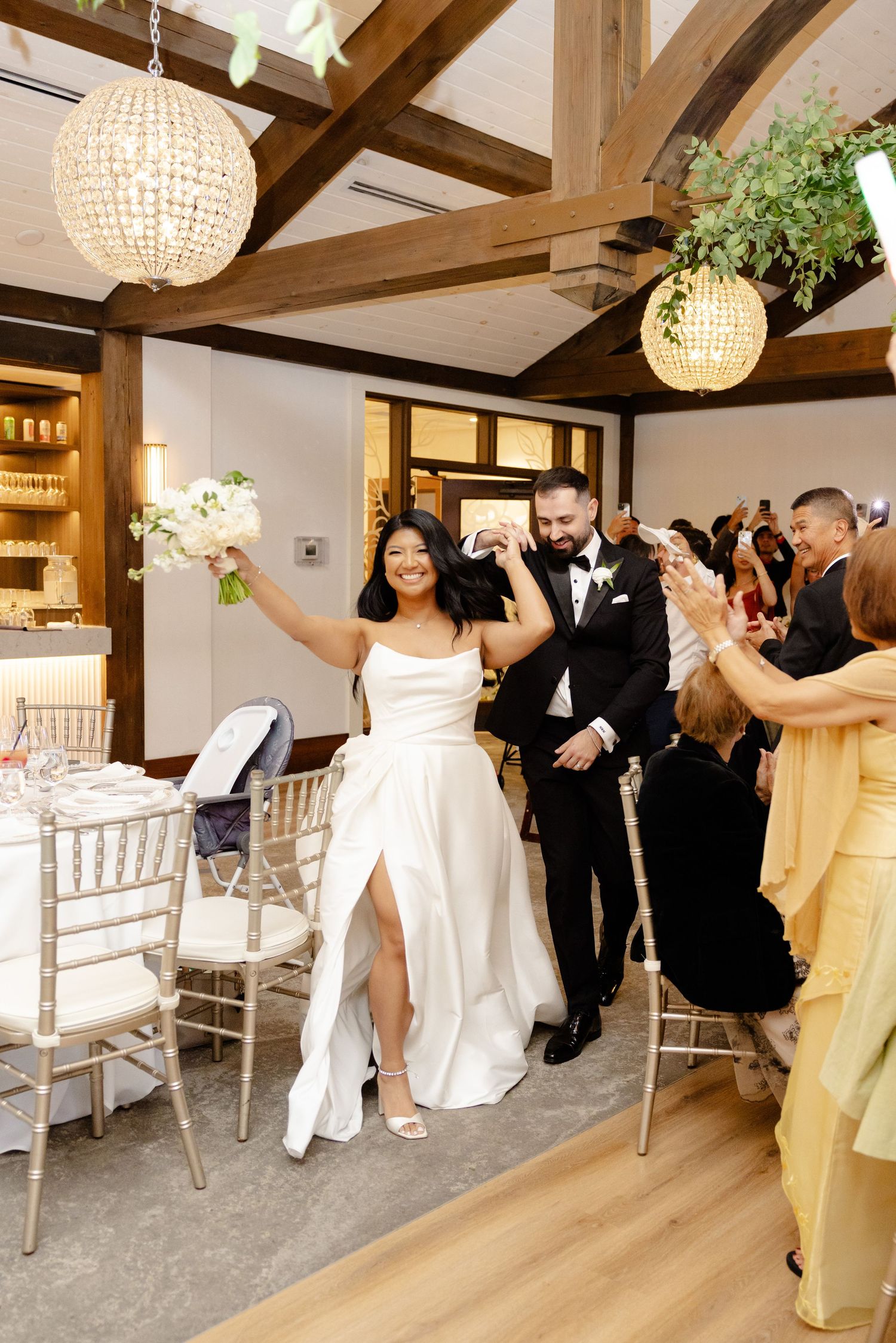 Wedding celebration in an elegant venue with exposed beams and crystal chandeliers.