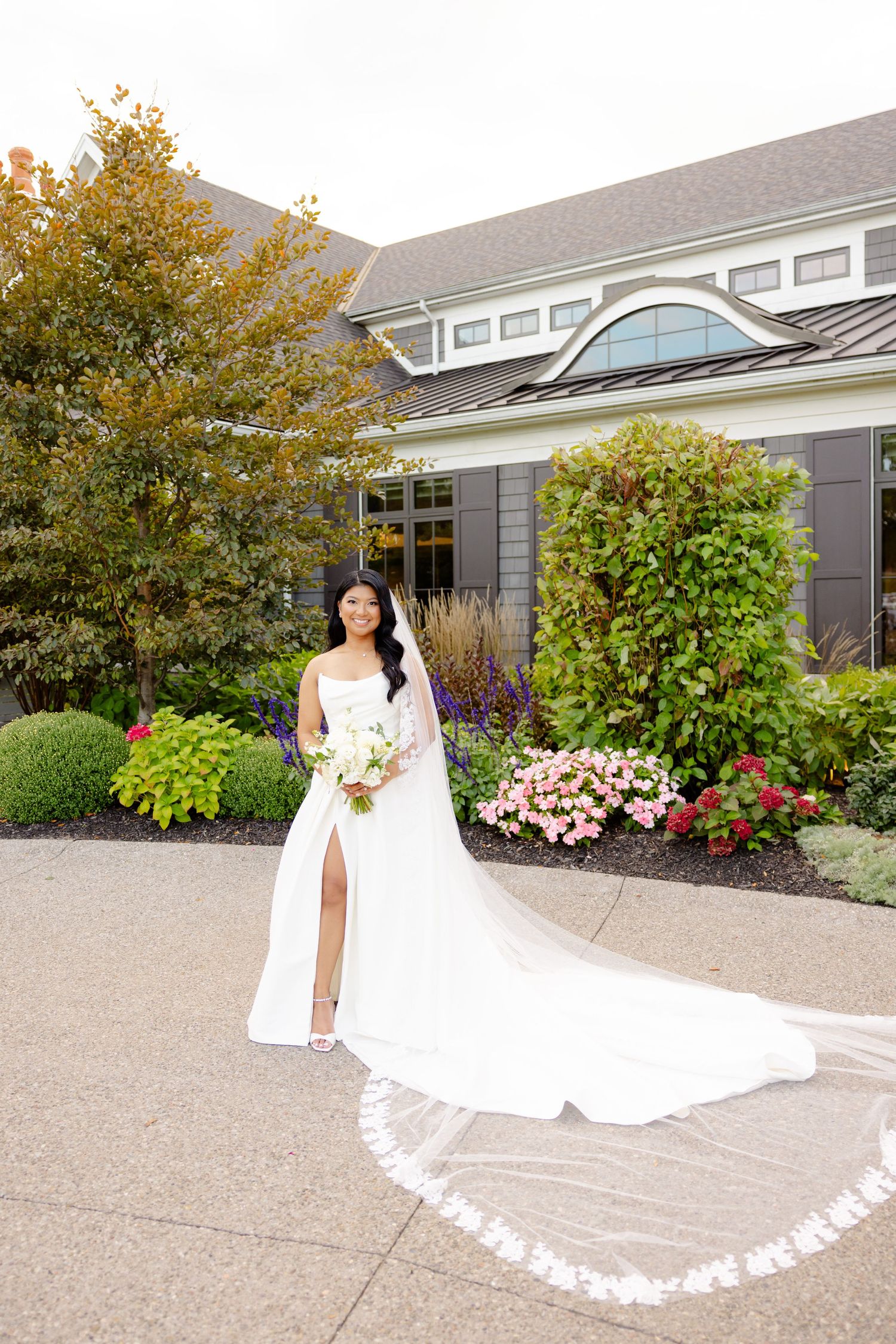 Elegant bridal portrait showcasing a flowing white gown with cathedral veil against landscaped garden backdrop.