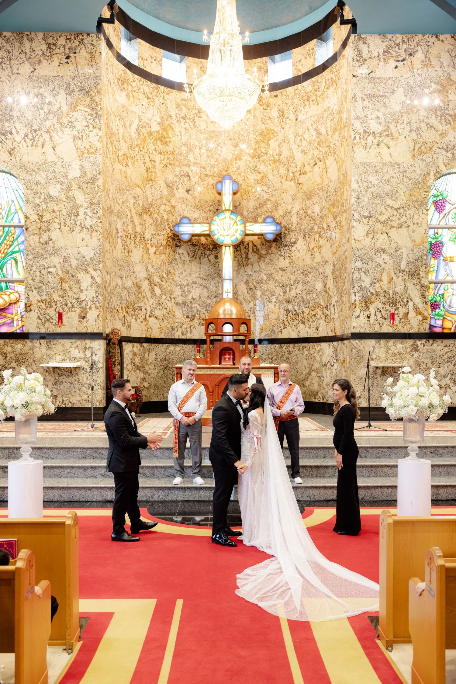 A wedding ceremony under crystal chandelier with cross and stained glass windows in elegant church setting.