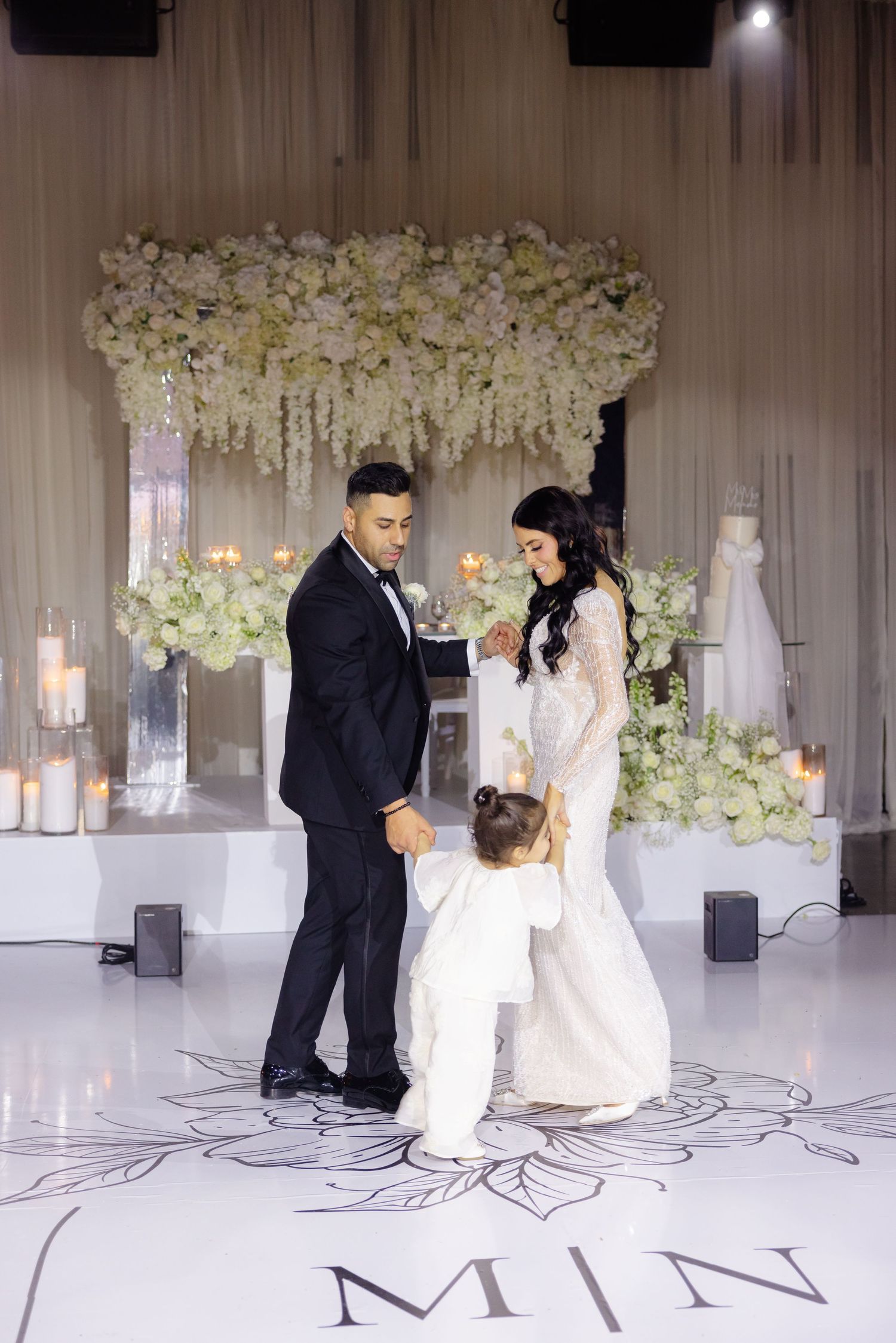 Wedding party poses on monogrammed dance floor with elegant white floral backdrop.