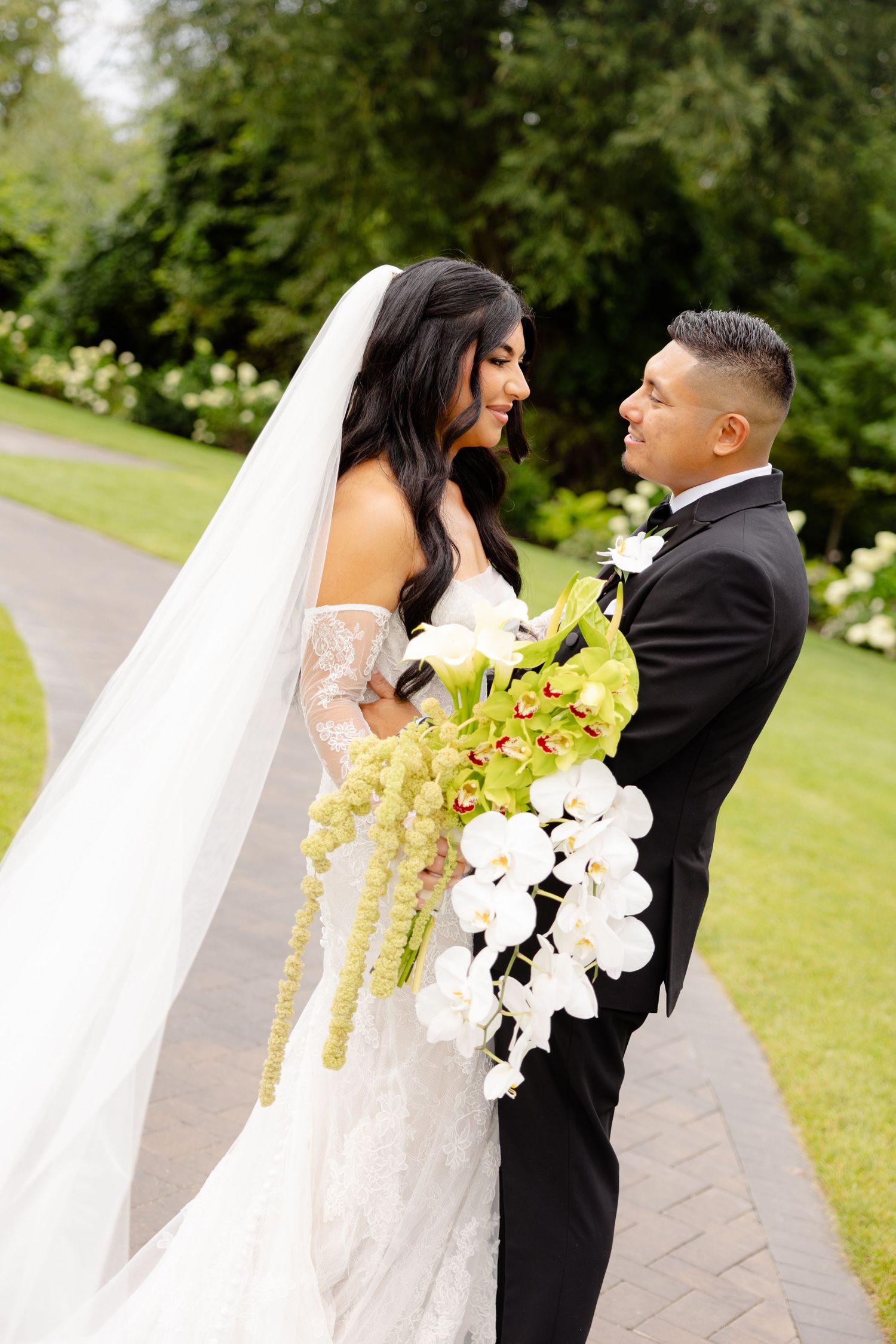 Newlywed couple embraces on garden path with bride holding elegant white and yellow orchid bouquet.