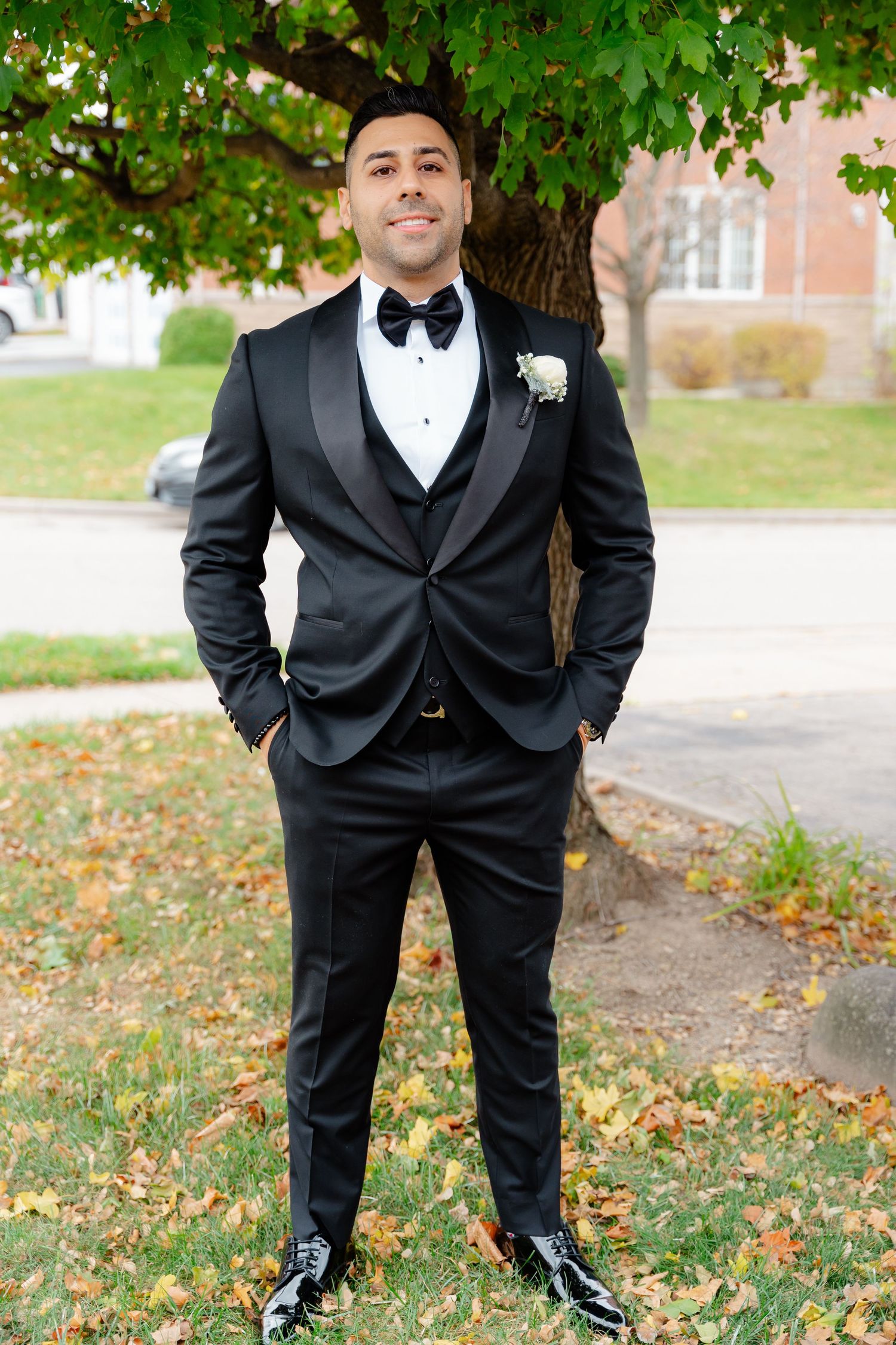 Full length shot of groom in formal black tuxedo standing in front of autumn tree.