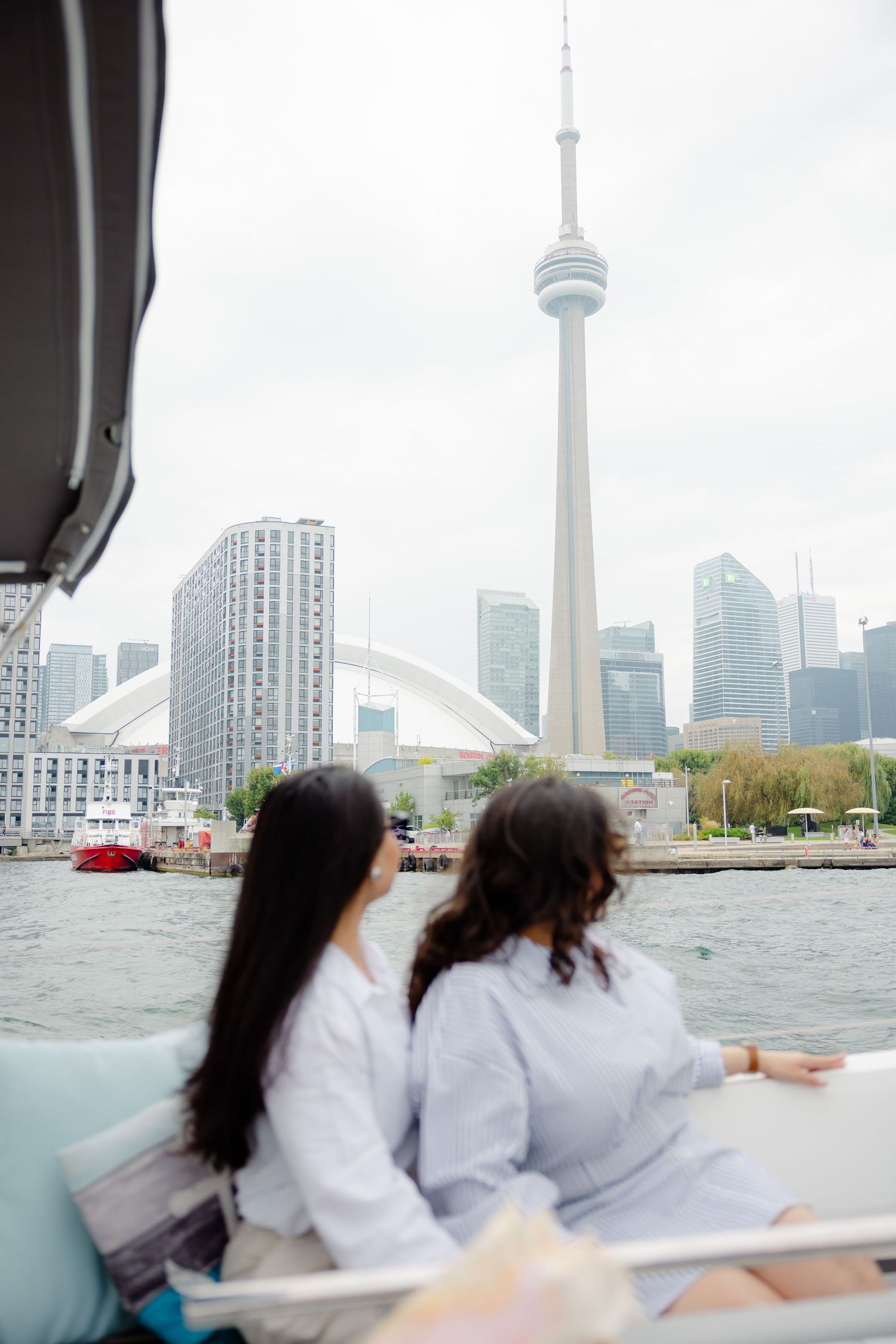 Two friends enjoy a boat ride with Toronto's iconic CN Tower and Rogers Centre visible in the skyline.
