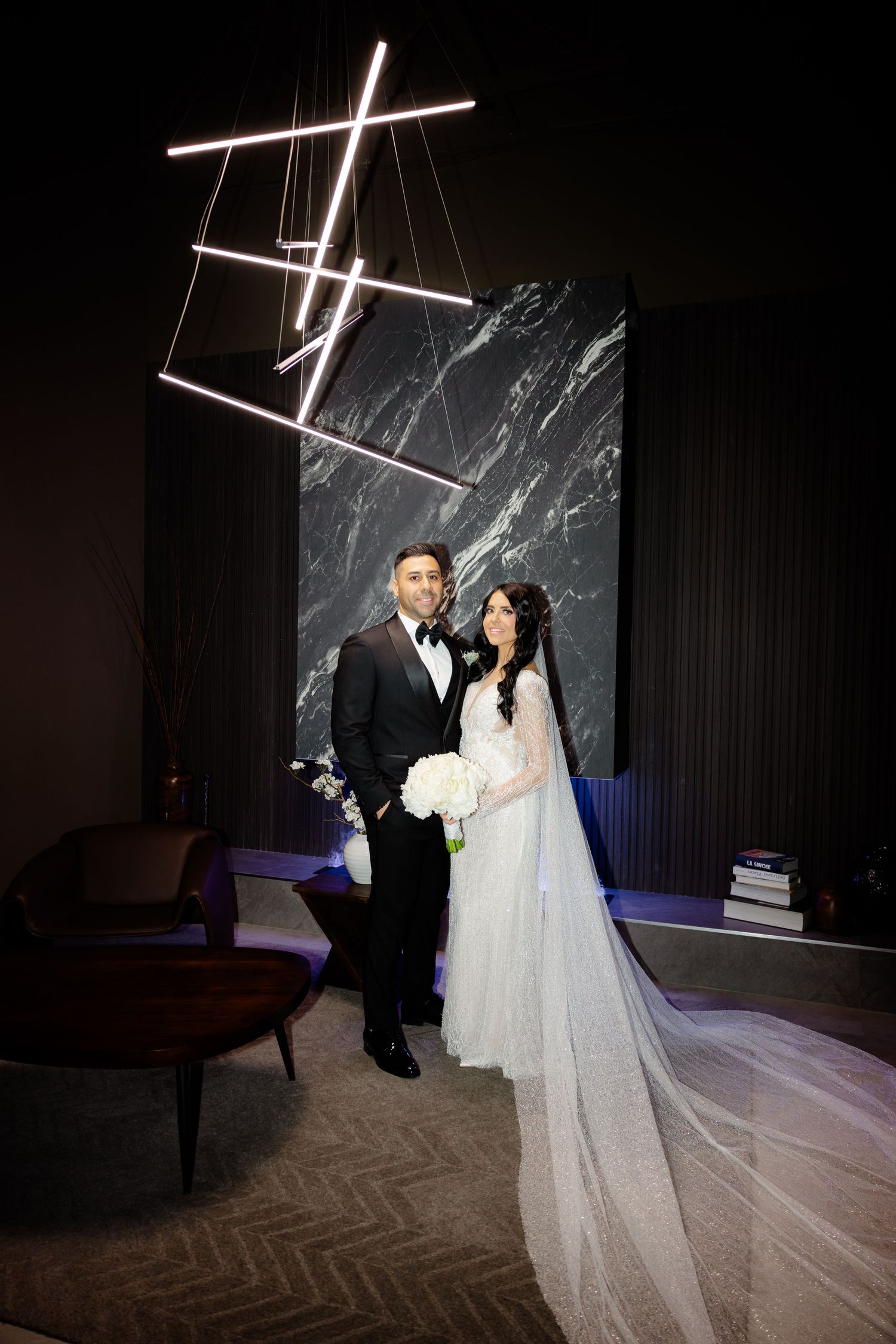 Elegant wedding portrait with geometric lighting installation and marble backdrop.