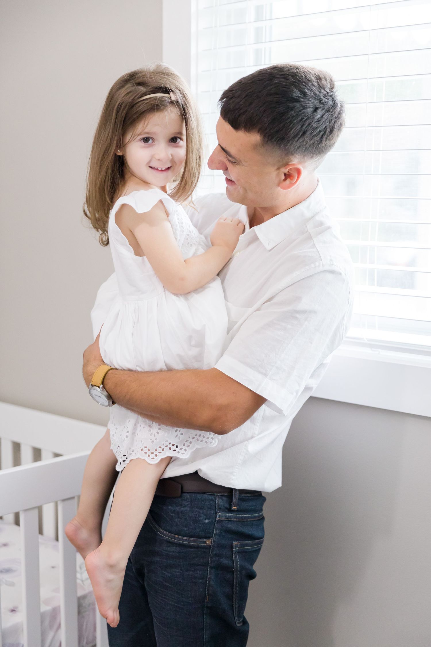 Parent and child share a loving moment by a window in white matching outfits.