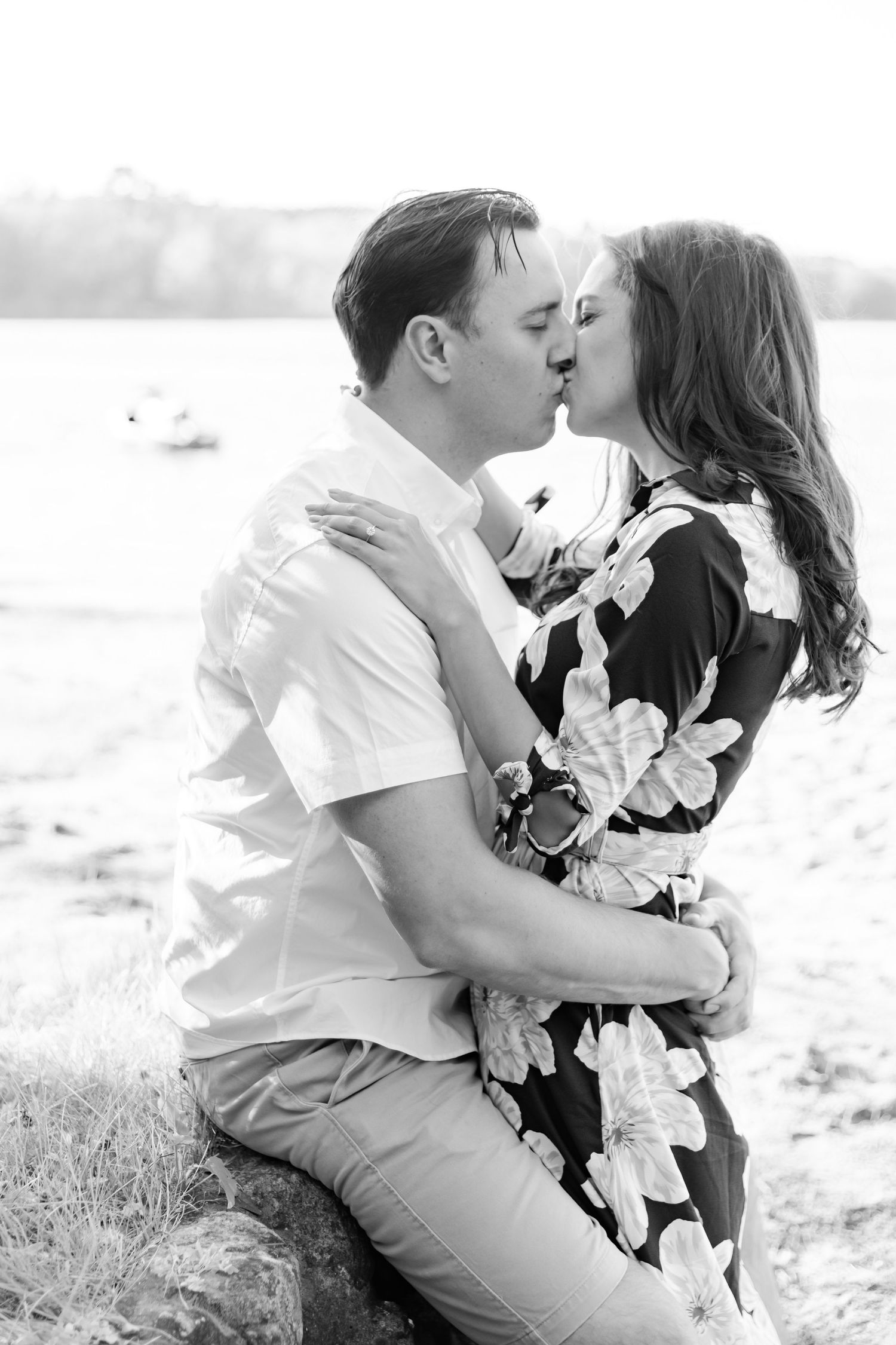 Black and white romantic portrait of a couple sharing an intimate kiss by the water.