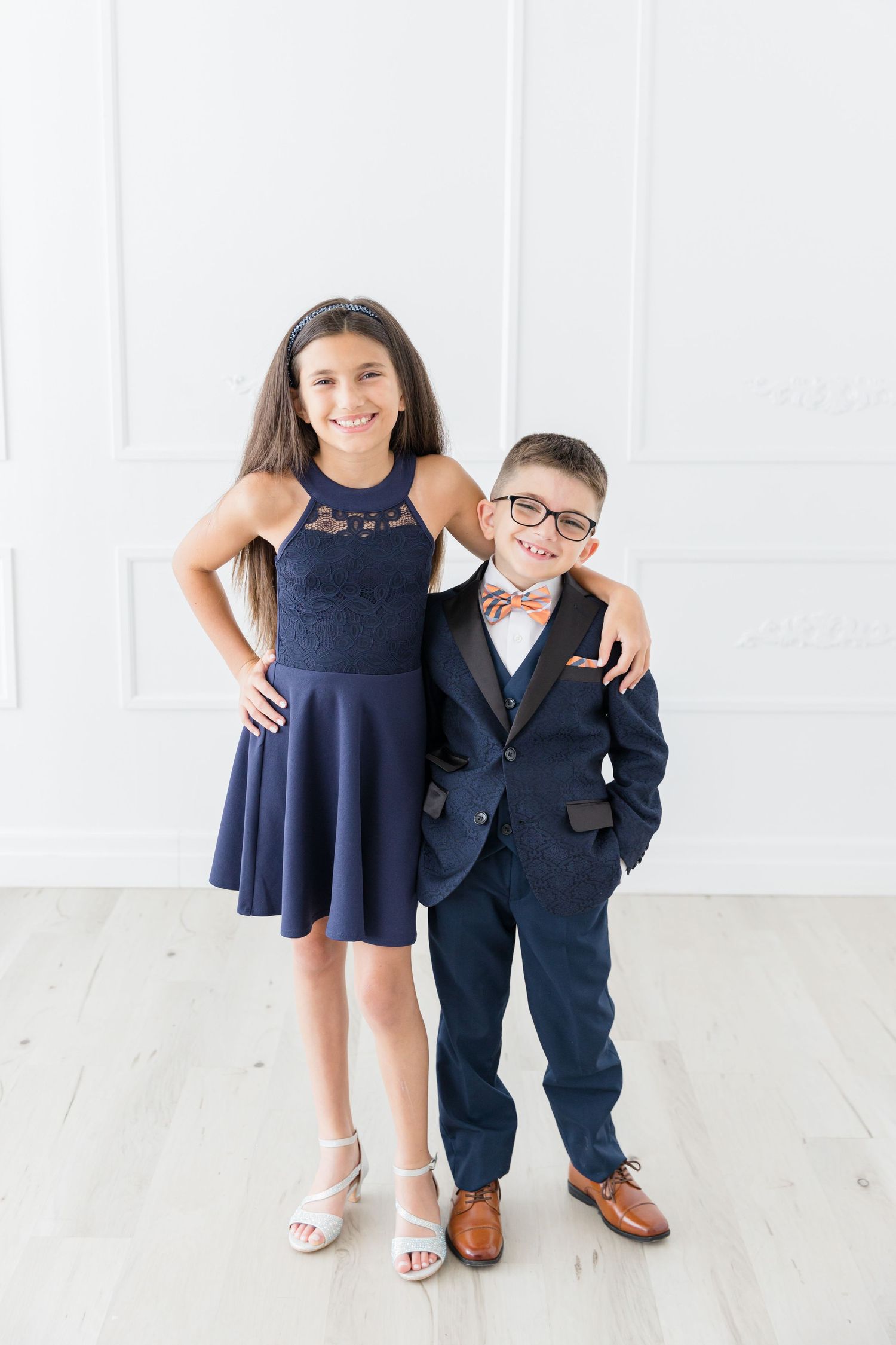 Two people dressed up in formal attire pose together against a white wall.