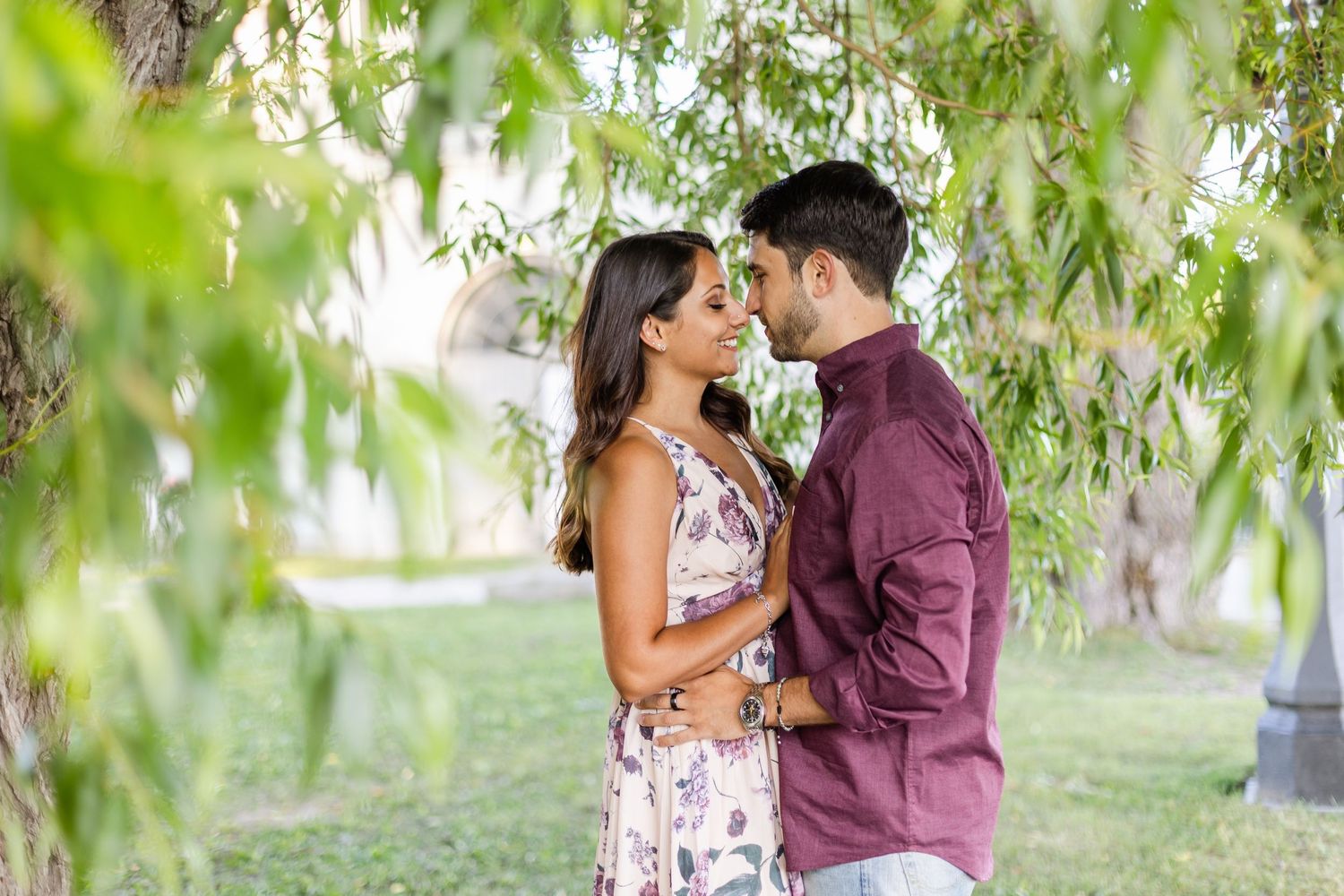 Couple sharing intimate moment under willow trees in coordinated spring outfits.
