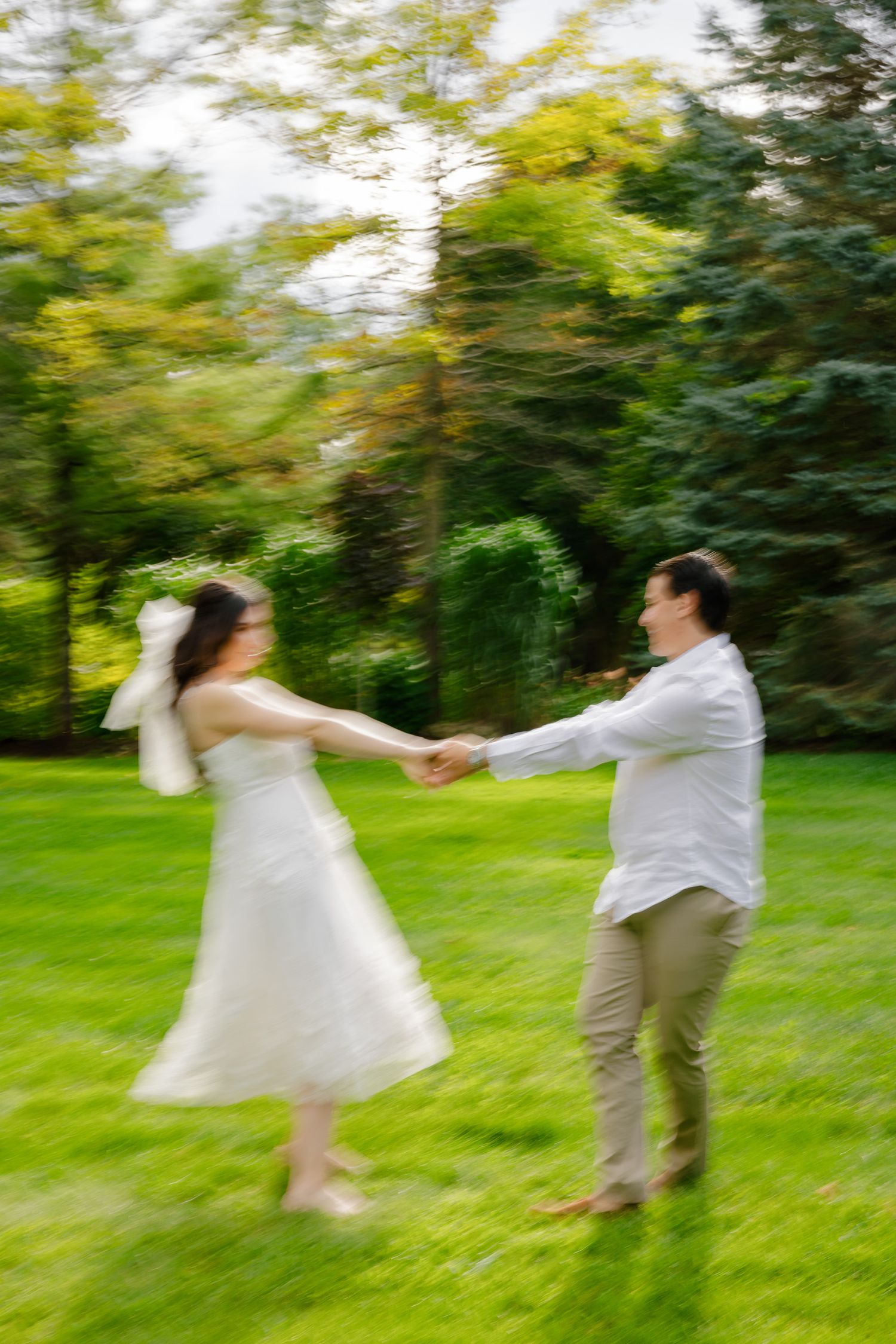 A motion-blurred photo of a couple dancing together on grass with trees in the background.