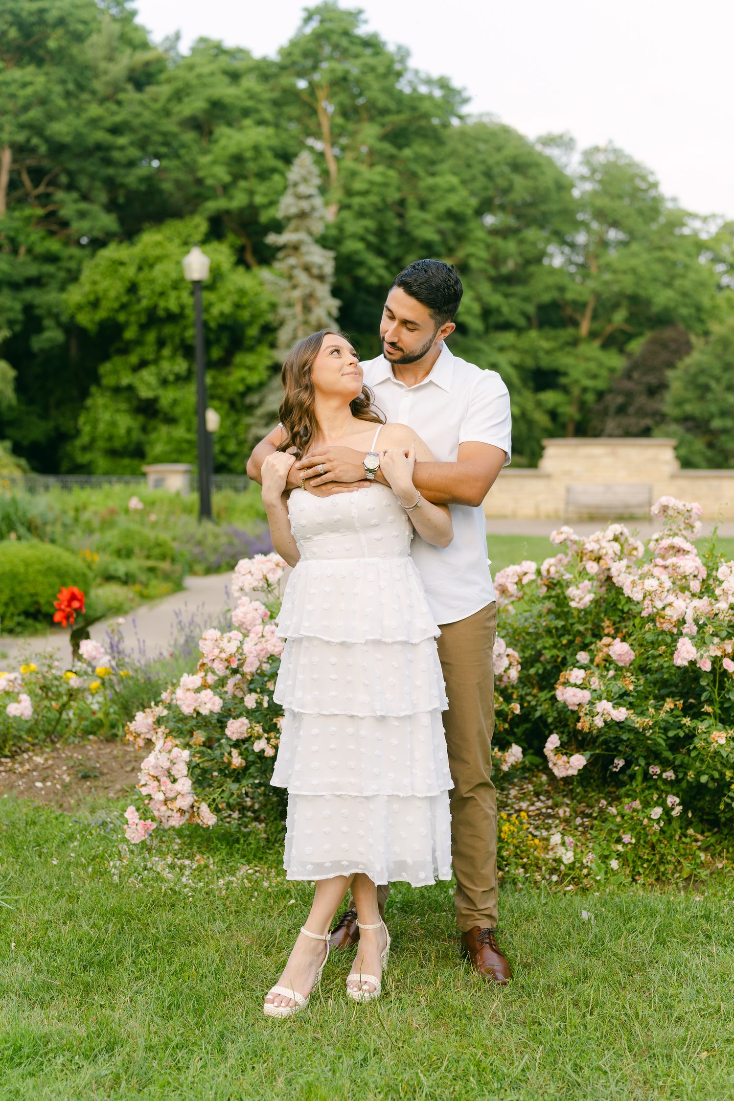 A couple shares a romantic moment in a garden setting with pink roses and greenery.