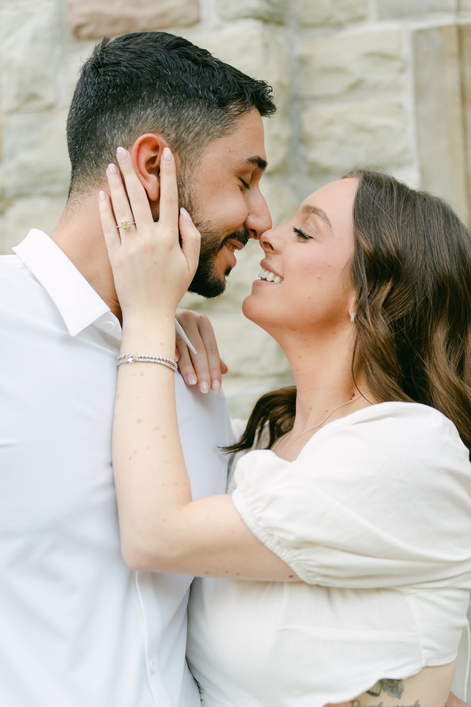 Close-up portrait of couple sharing intimate moment against light stone wall background.
