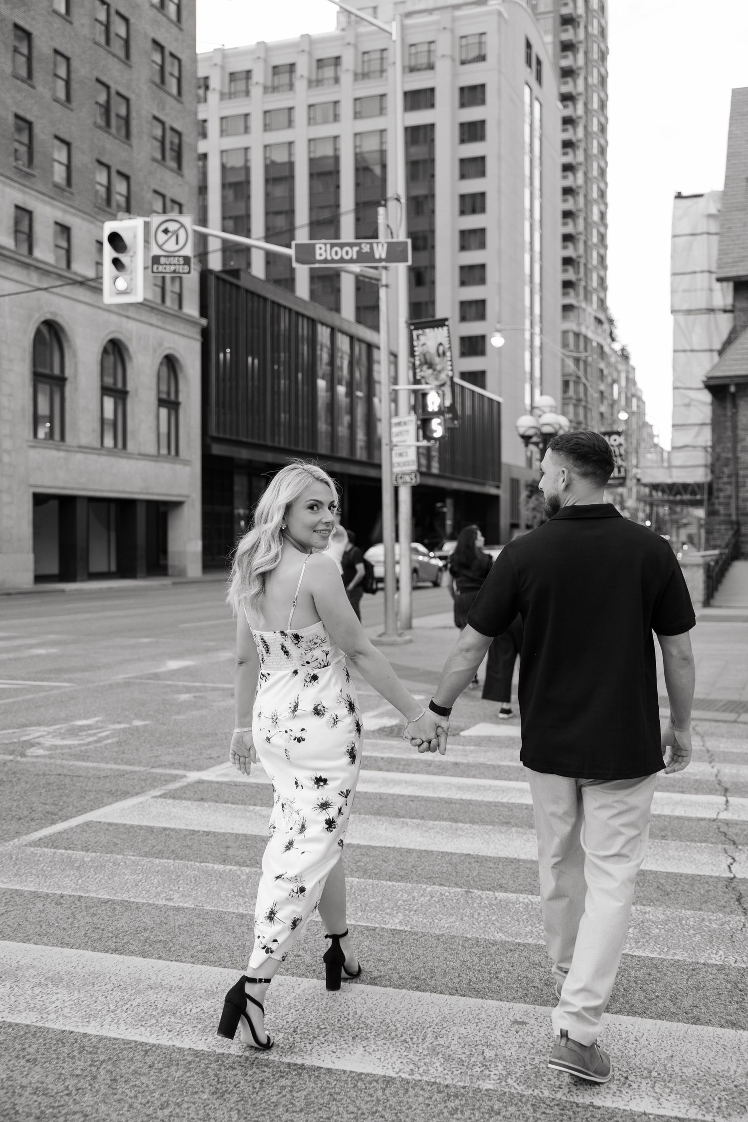 A couple walks hand in hand across a downtown intersection in monochrome.