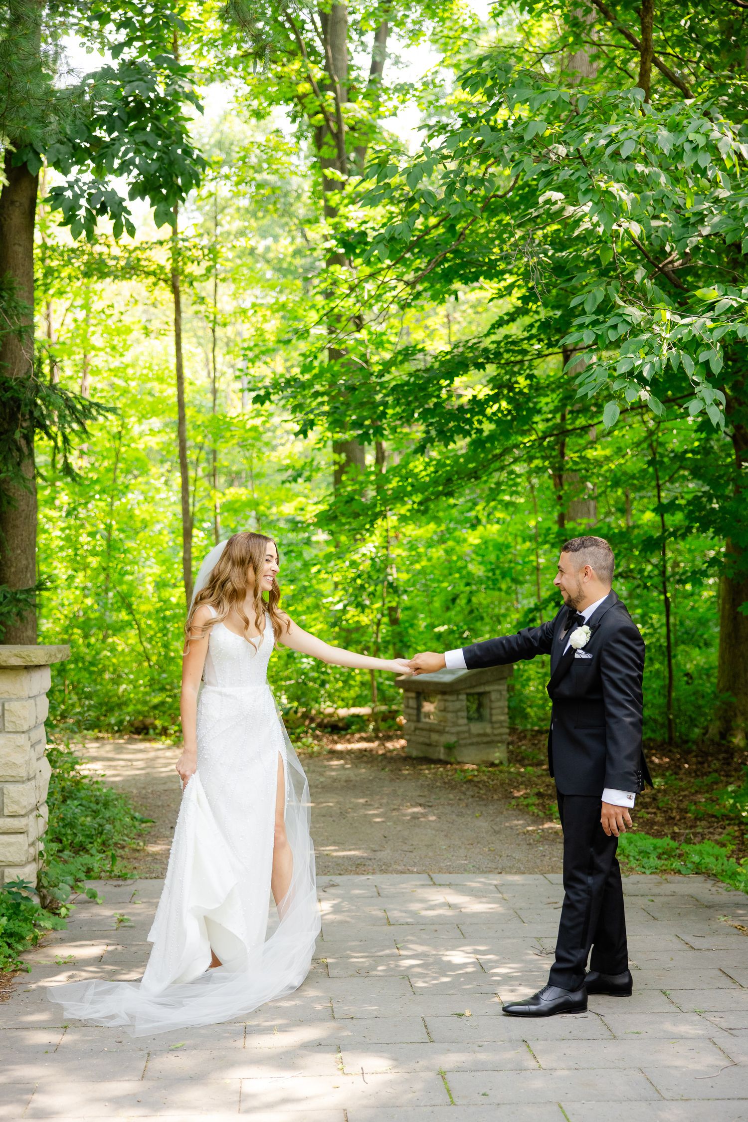 Couple in wedding attire sharing a dance move on a stone path with green foliage background.