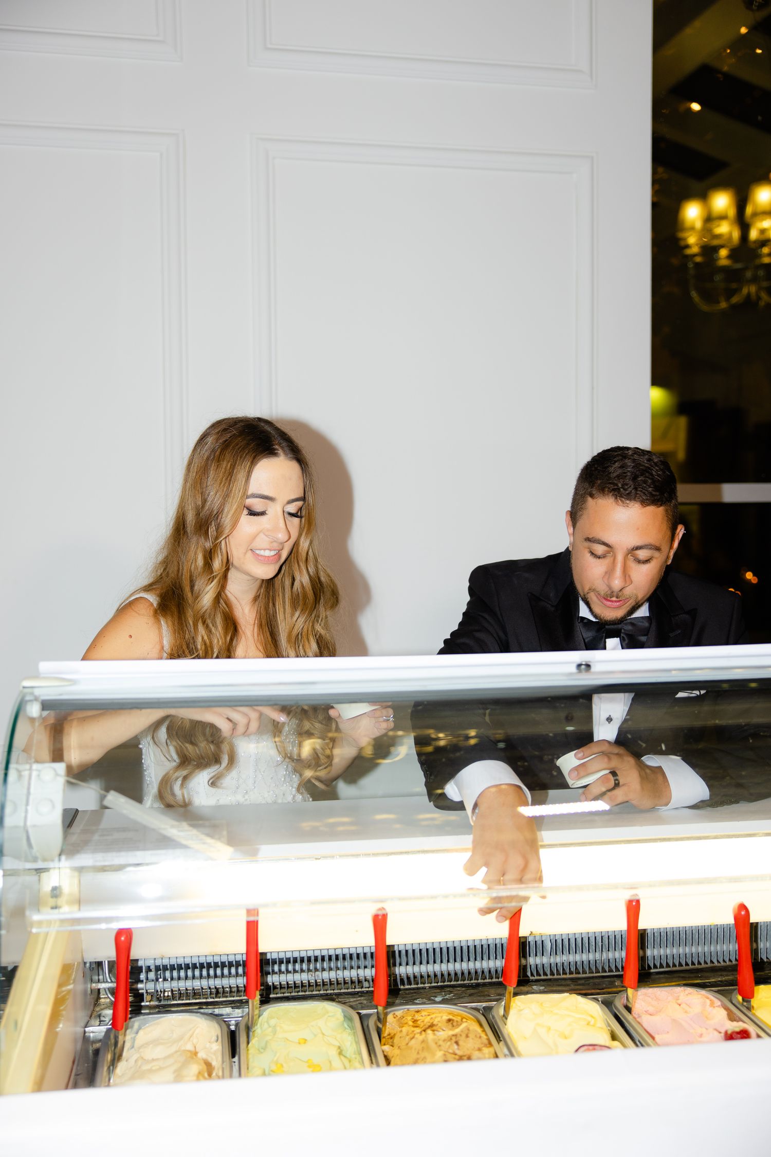 Couple selecting ice cream flavors from a display case at their wedding reception.