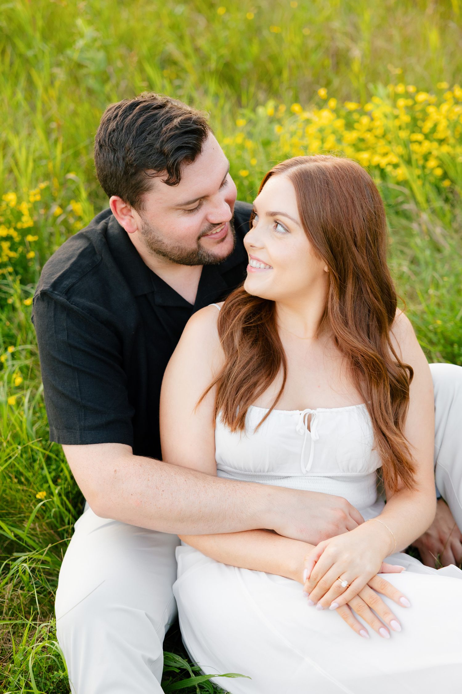 Intimate moment between couple sitting in flowering meadow during summer.