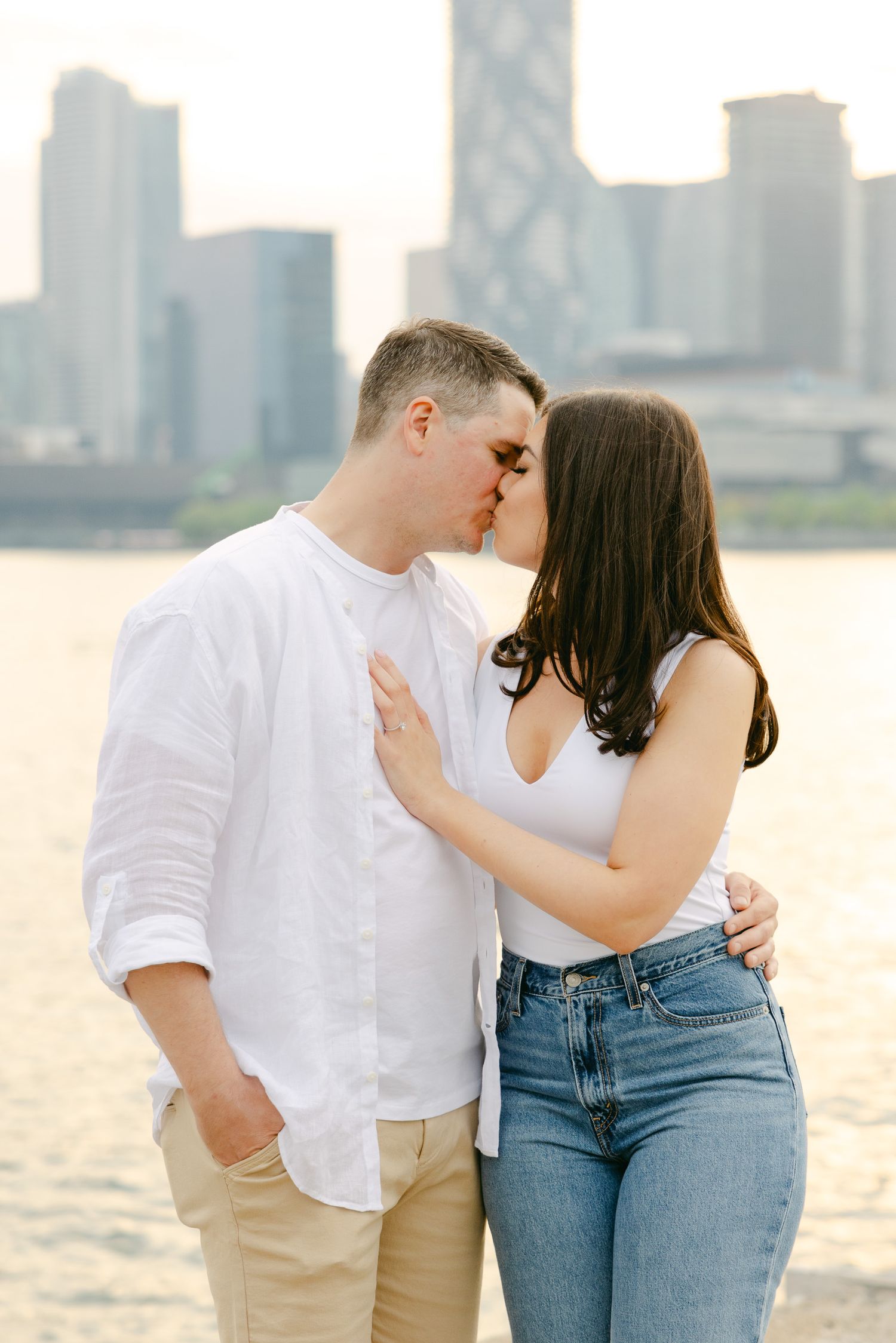Intimate moment between couple on wooden pier with Toronto's urban skyline in soft sunset light.
