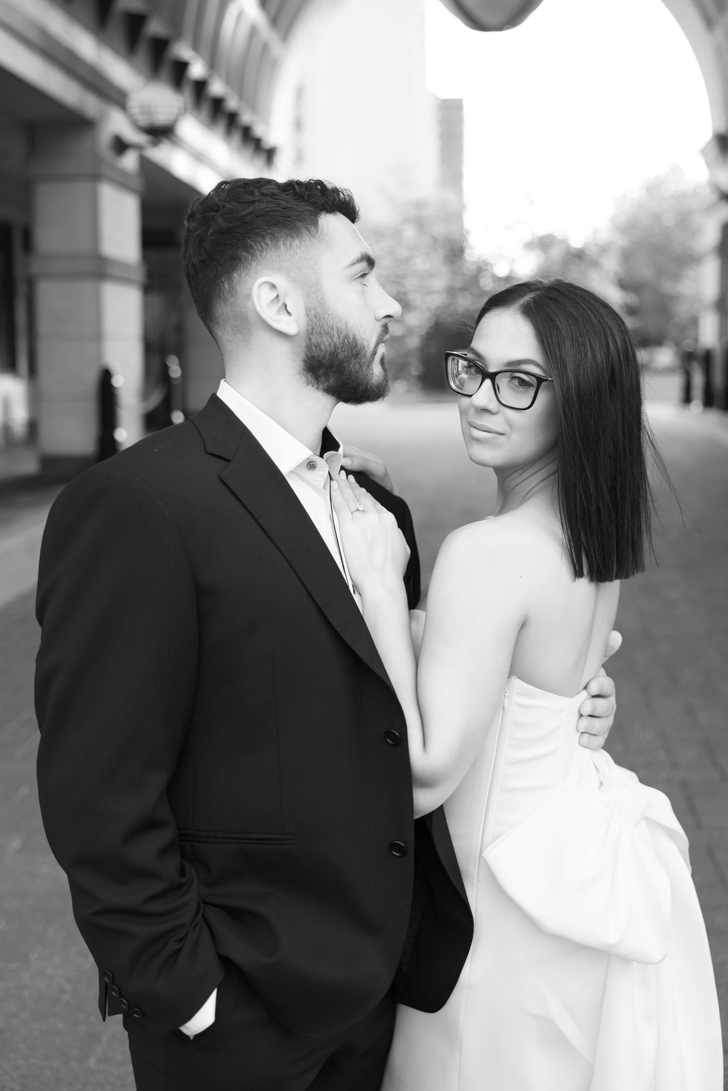 Black and white portrait of a stylishly dressed couple sharing a tender moment outdoors.