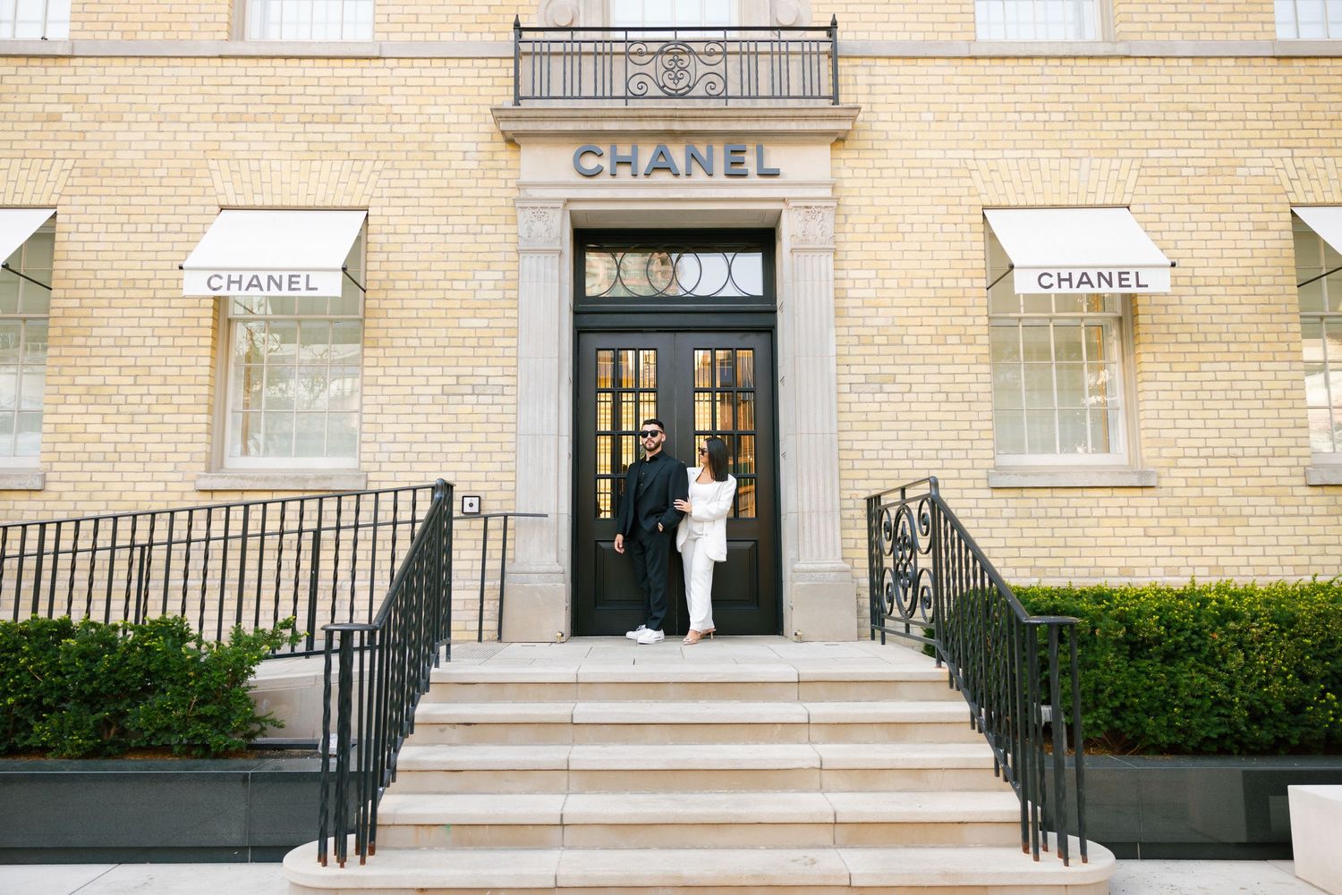 Wide shot of a couple posing at entrance of Chanel store with ornate architecture.