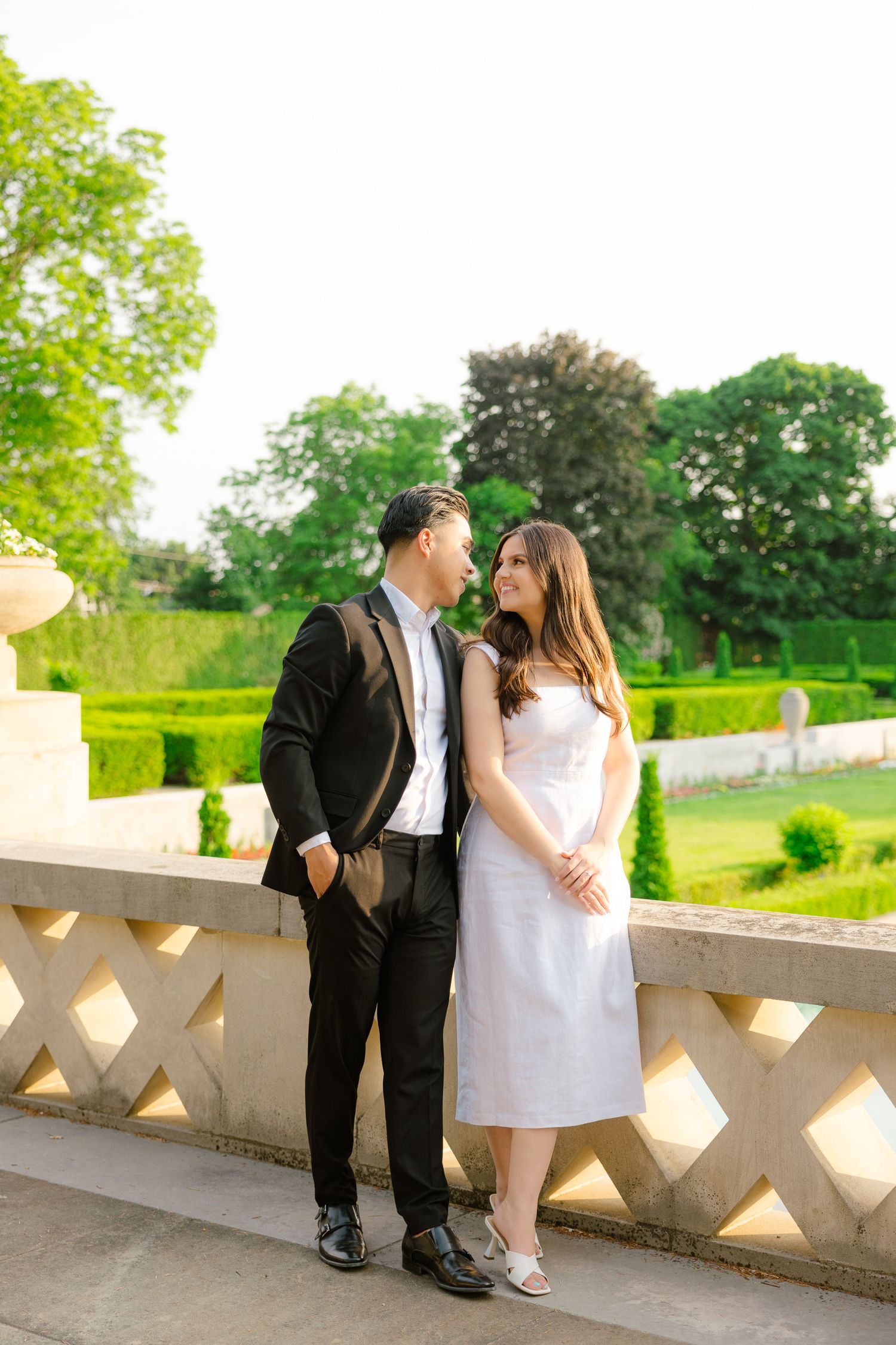 A couple sharing a tender moment on a sunny terrace overlooking manicured gardens.
