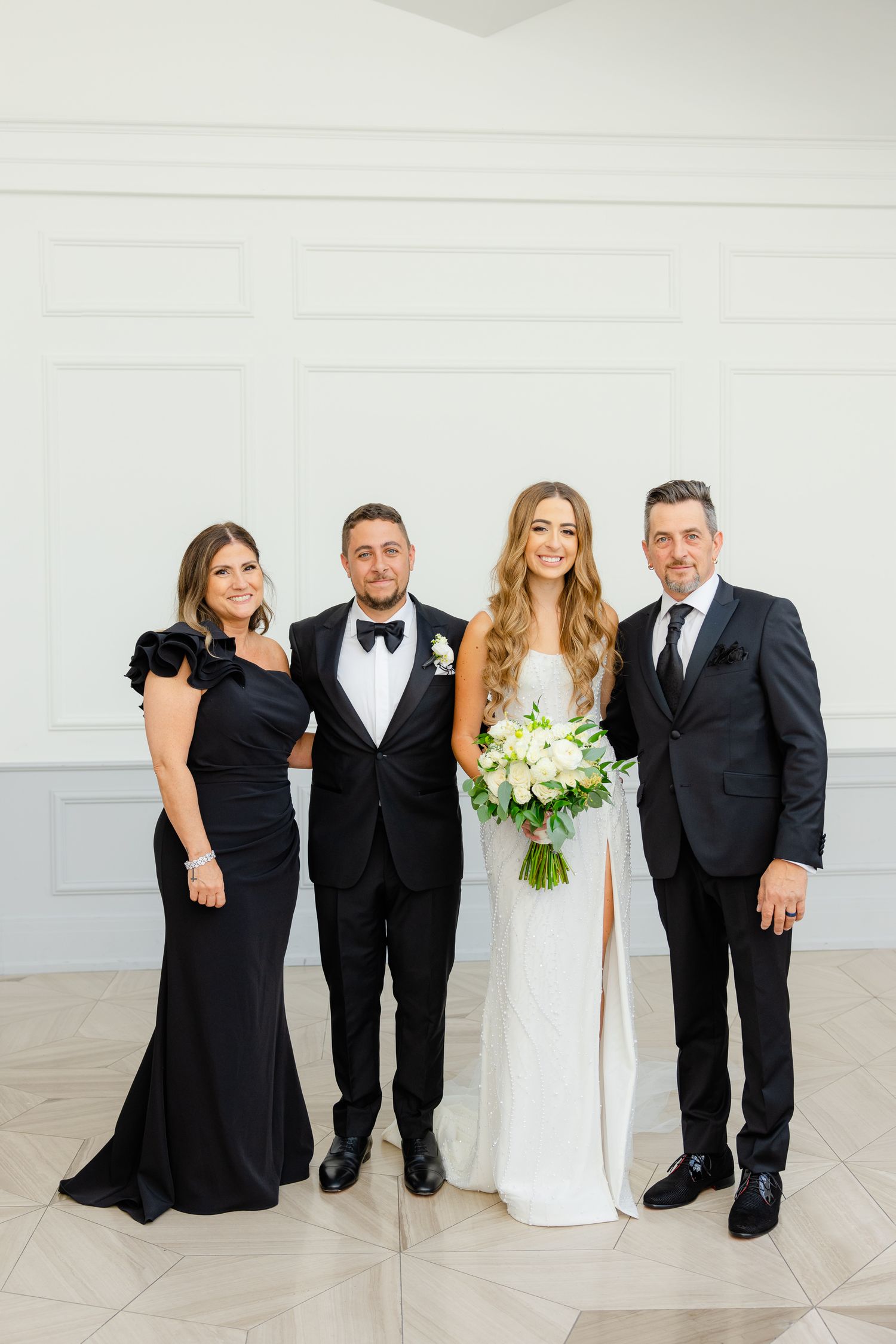 Wedding party members pose in formal attire with the bride holding a white and green bouquet.