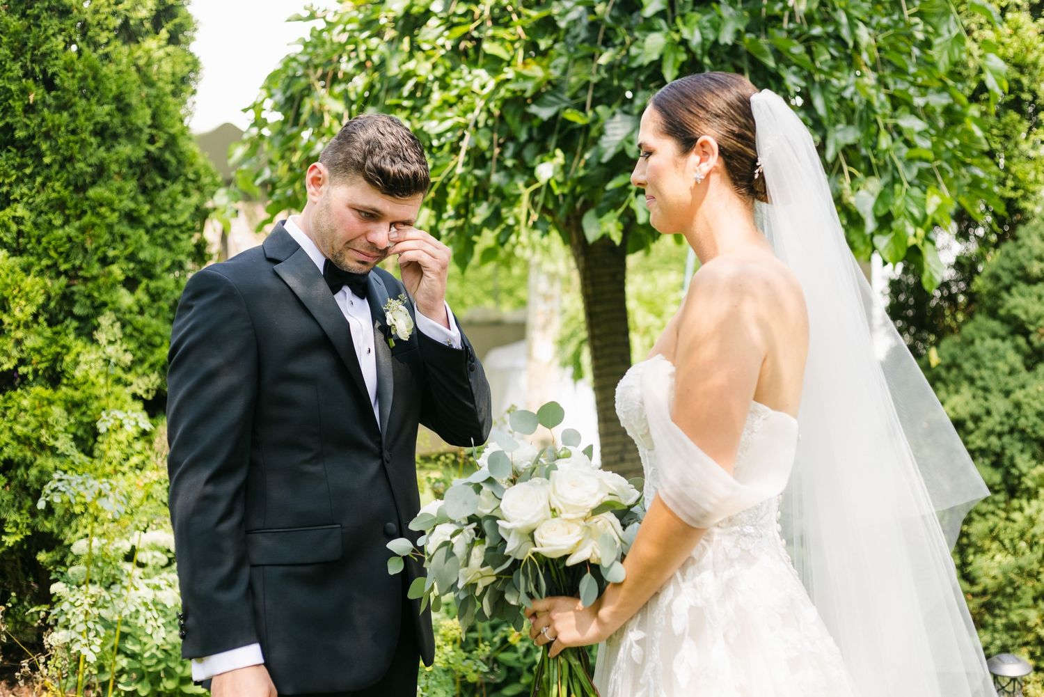 Emotional wedding couple wipes away tears during their first look in a garden setting.