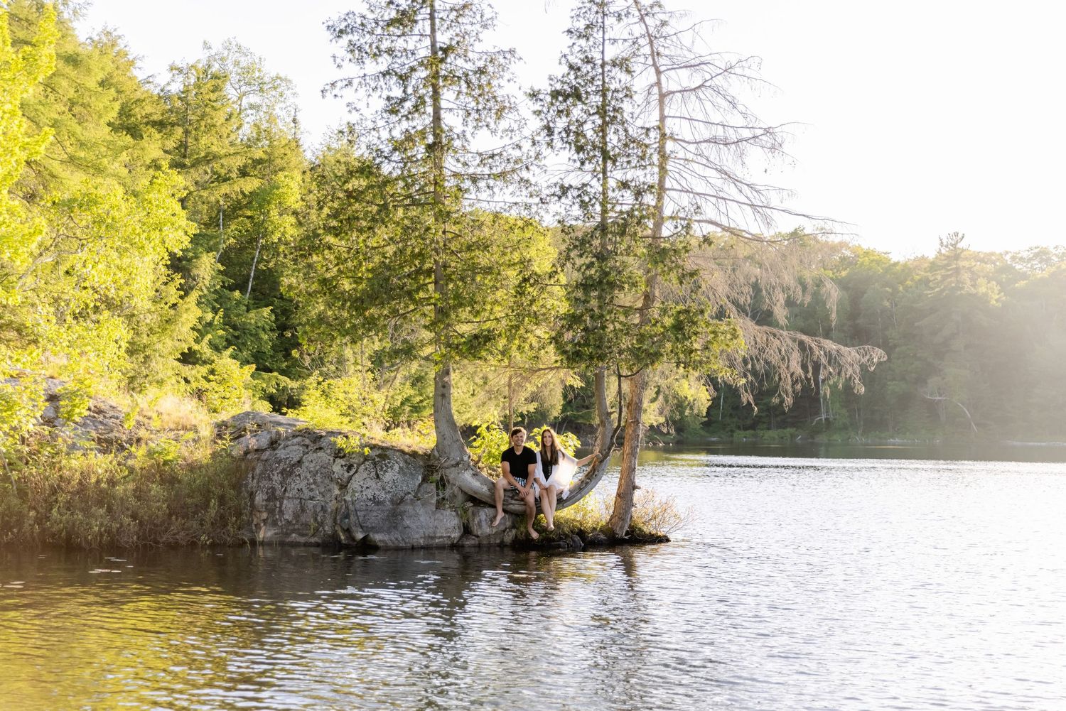 Scenic lakeside moment captured with sunlight filtering through trees around a rocky outcrop.